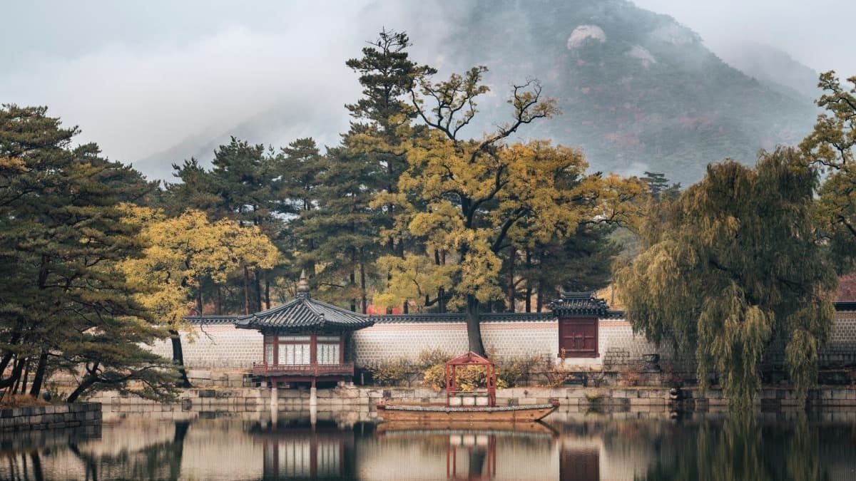 Brown and white house near green trees and lake in front of foggy mountain during daytime
