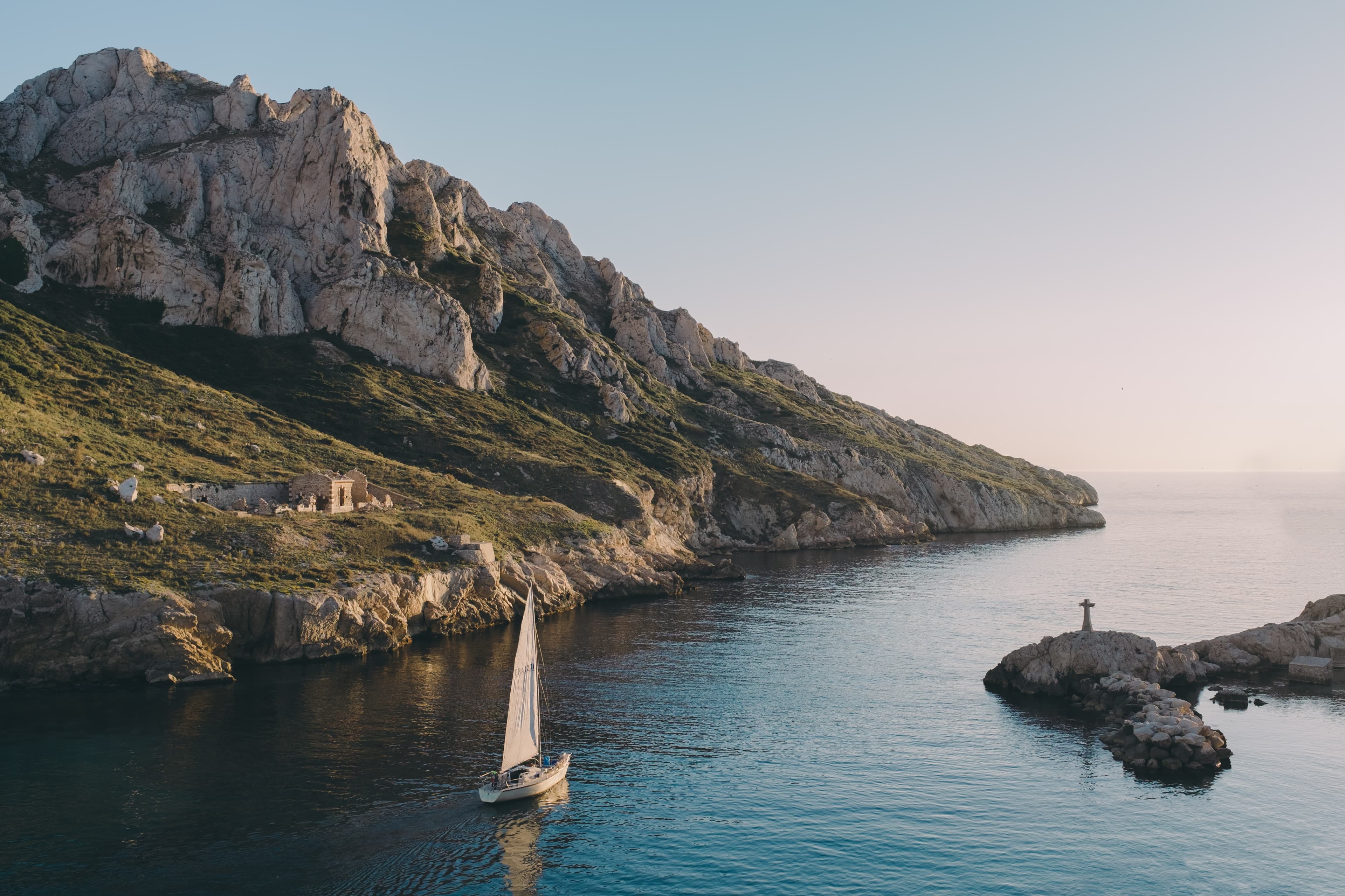 blue ocean water with brown stone cliffs and green grass with a white sailboat