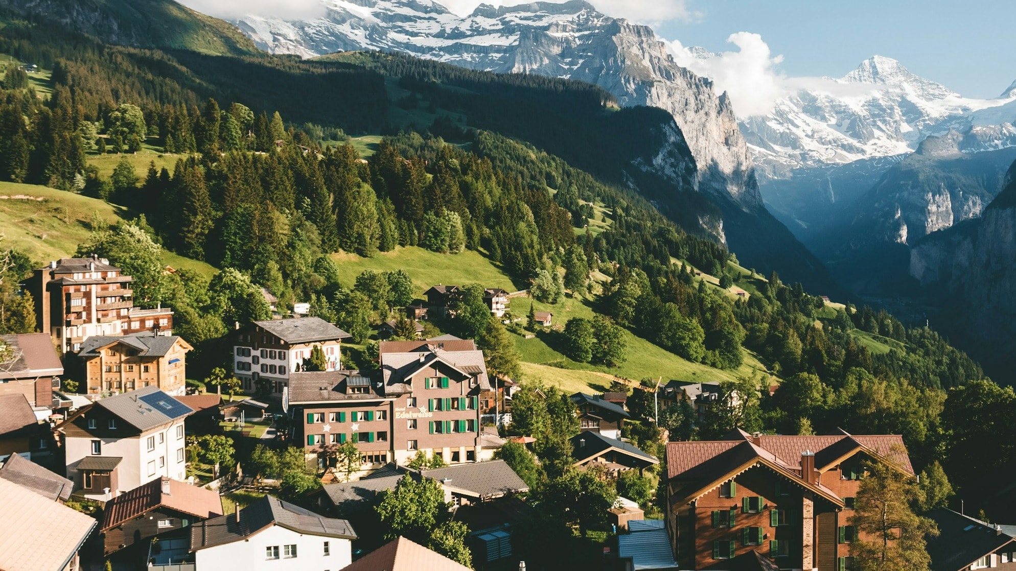 A sloping hillside with picturesque buildings, lush green landscape and snow-capped mountains in the distance