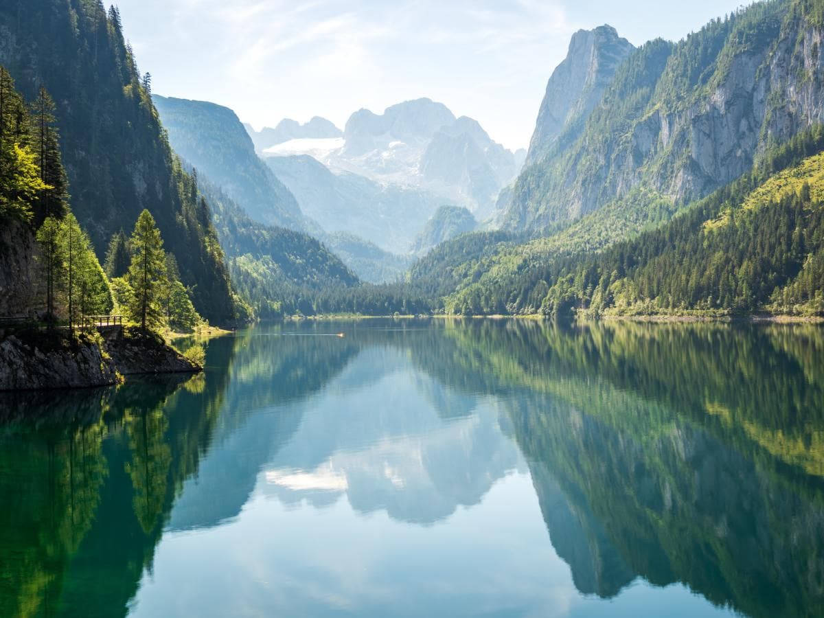 Blue lake water surrounded by green trees and tall white snowcapped mountains