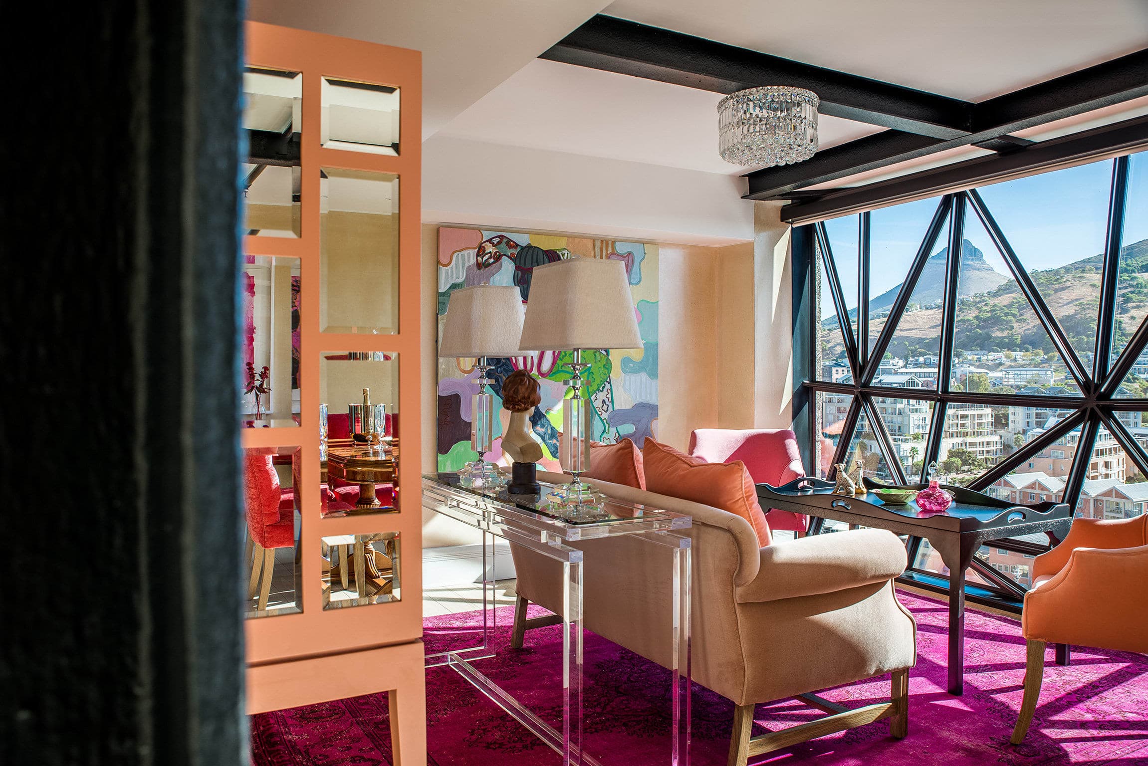 a luxe hotel room with a pink rug and a couch overlooking a city