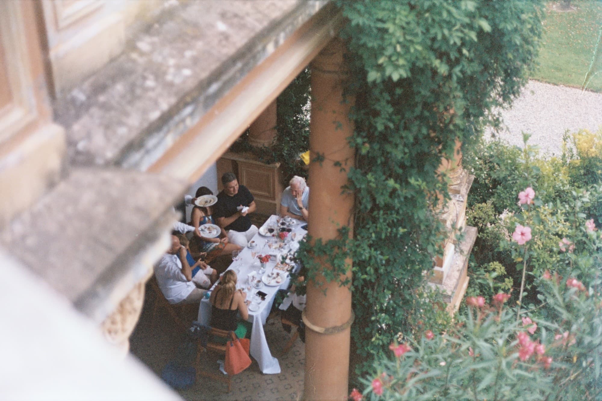 view from above of people enjoying dinner at a long table covered in a white tablecloth