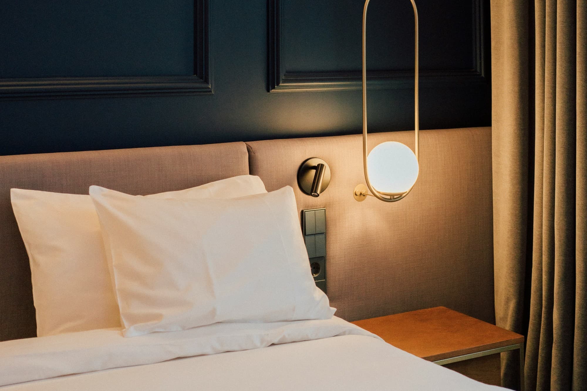 a white bed against a blue wall and a hanging gold lamp