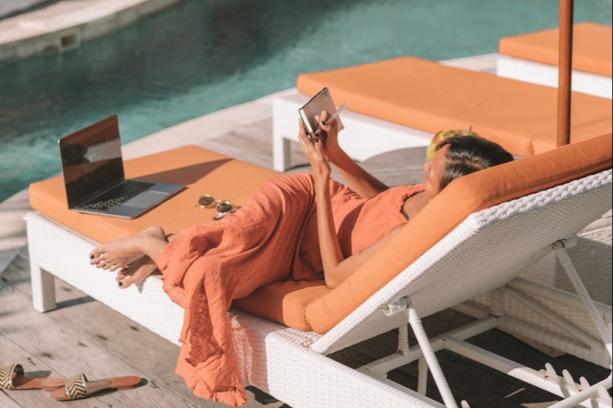 woman writing in her journal while lounging near a pool