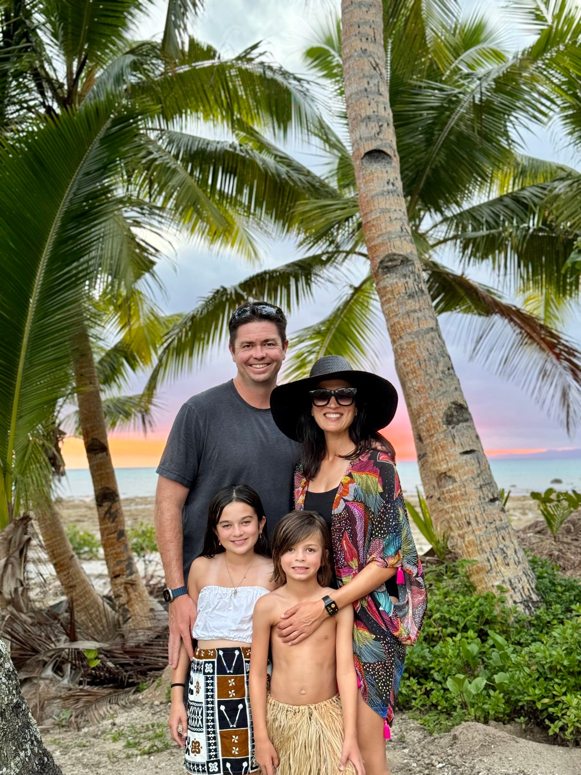 a man, a woman, and two young children stand in front of a palm tree