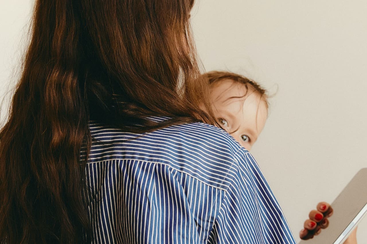 a woman in a blue striped shirt holds a baby in one arm and a tablet in the other