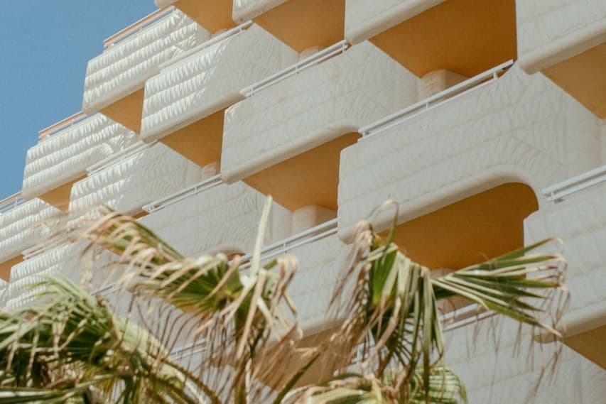 low-angle shot of a cream-covered hotel with palm leaves out front