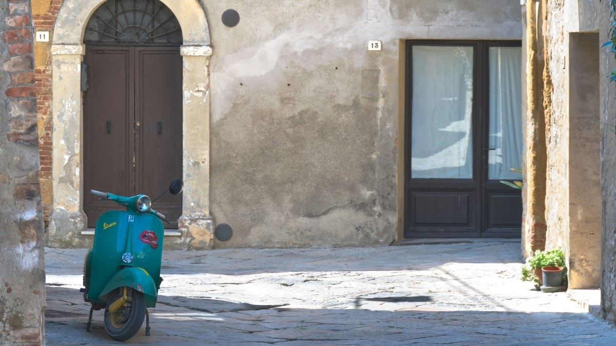 A Vespa parked on a narrow cobblestone street.