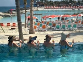 Four friends in the pool near the beach with drinks in hand.