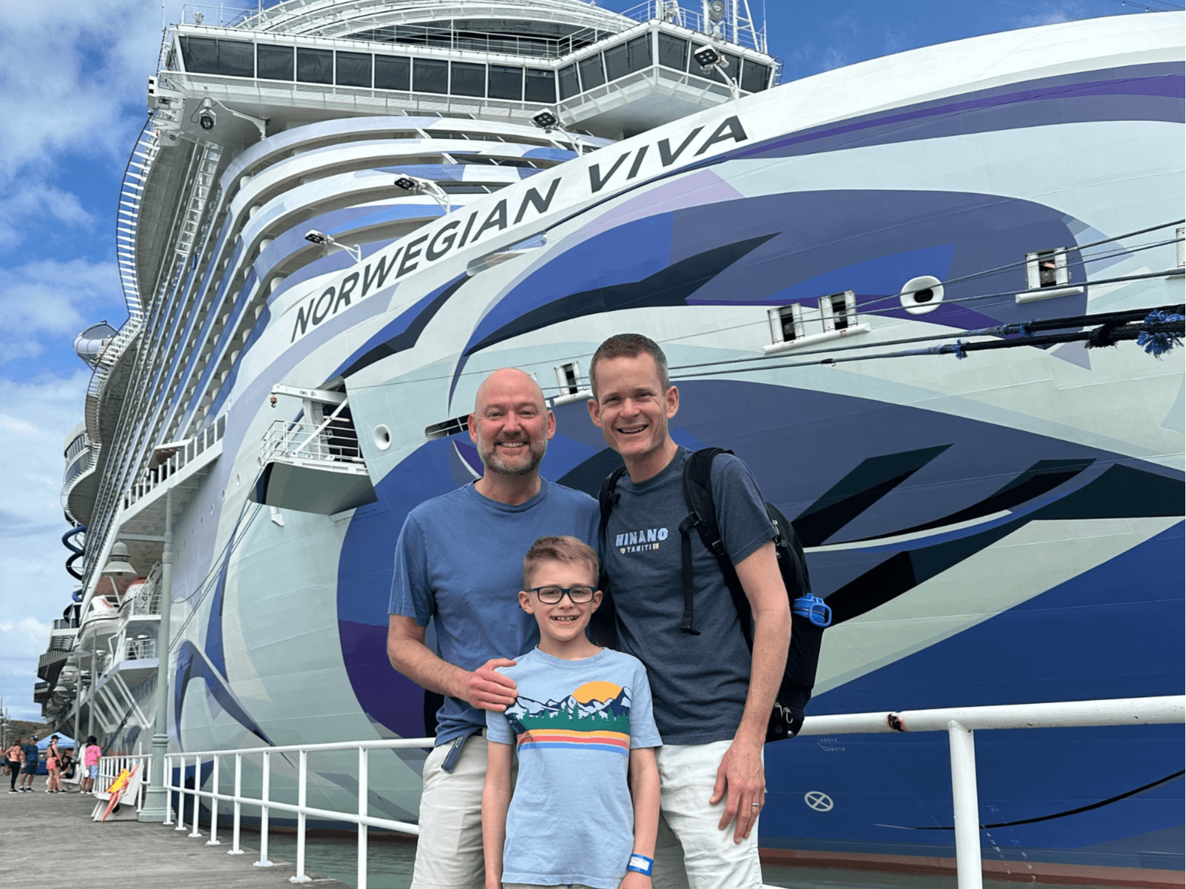 A father and two sons stand in front of a cruise ship.