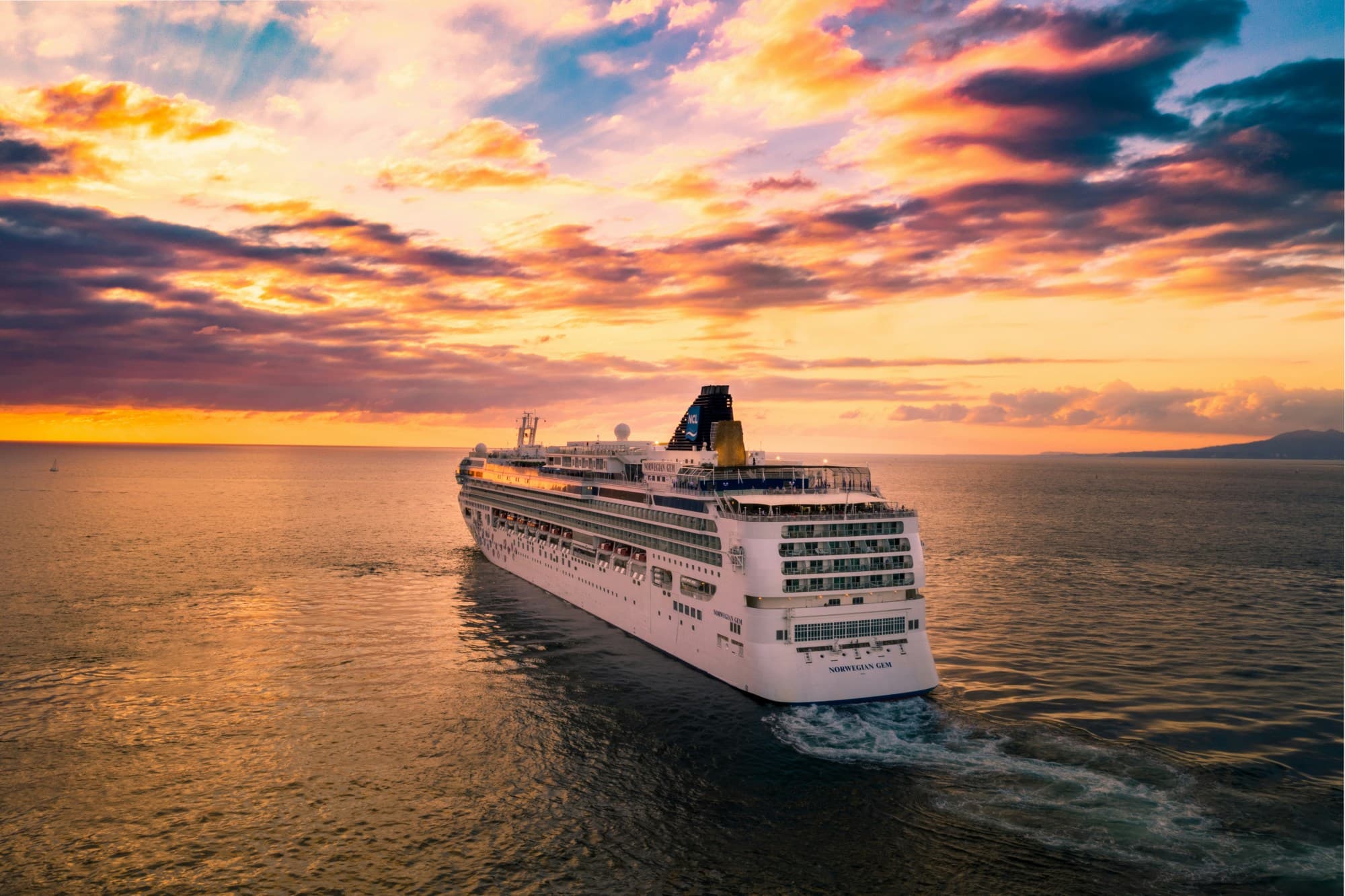 View of a cruise ship on the ocean with a purple and yellow sunset in the background.