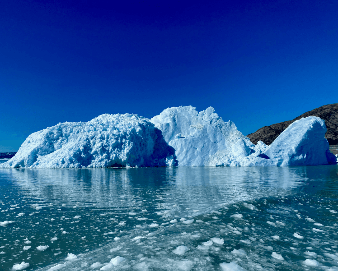 A view of a large ice glacier and icy ocean against a clear blue sky.