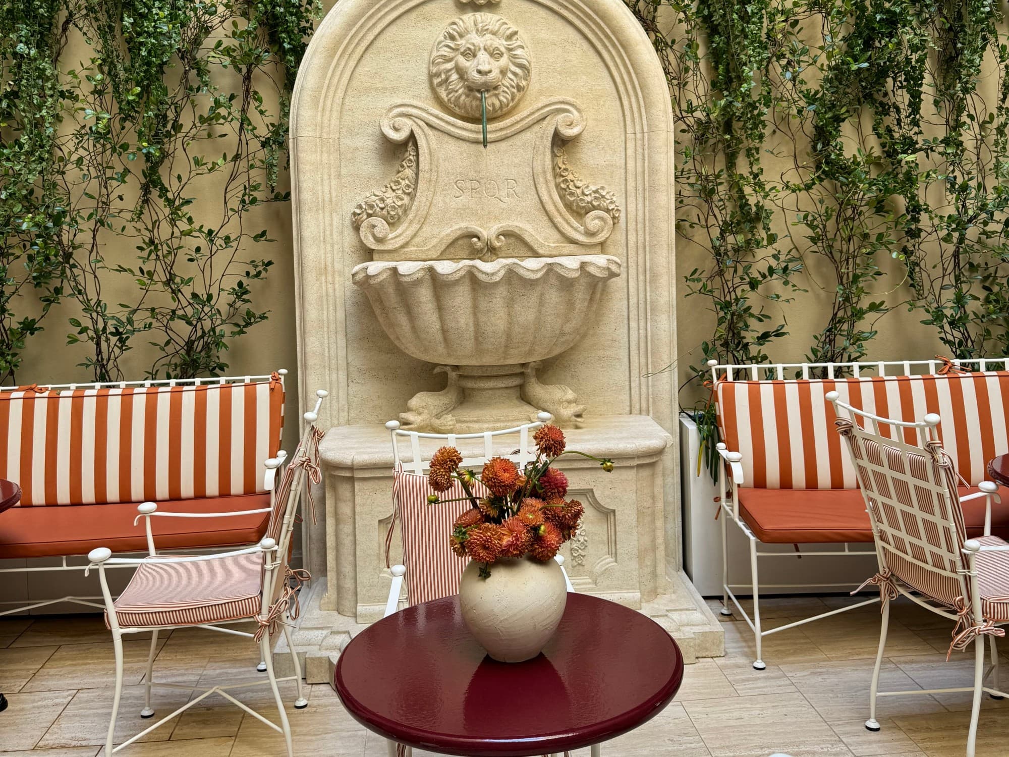 The hotel fountain flows in the courtyard surrounded by quaint, striped furnishings as vines hang down the brick wall.