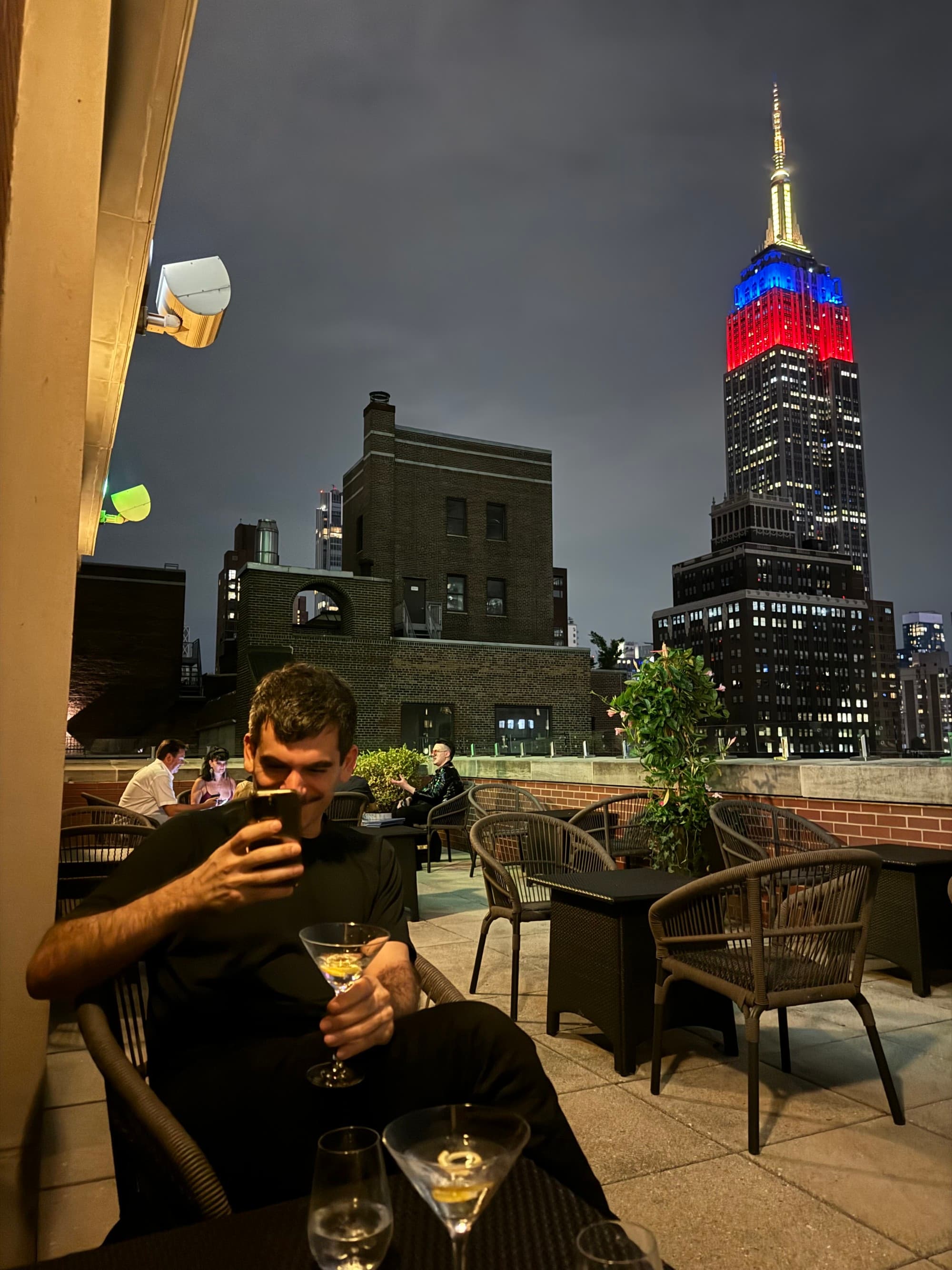 A man posing with a cocktail and the Empire State building in the distance.