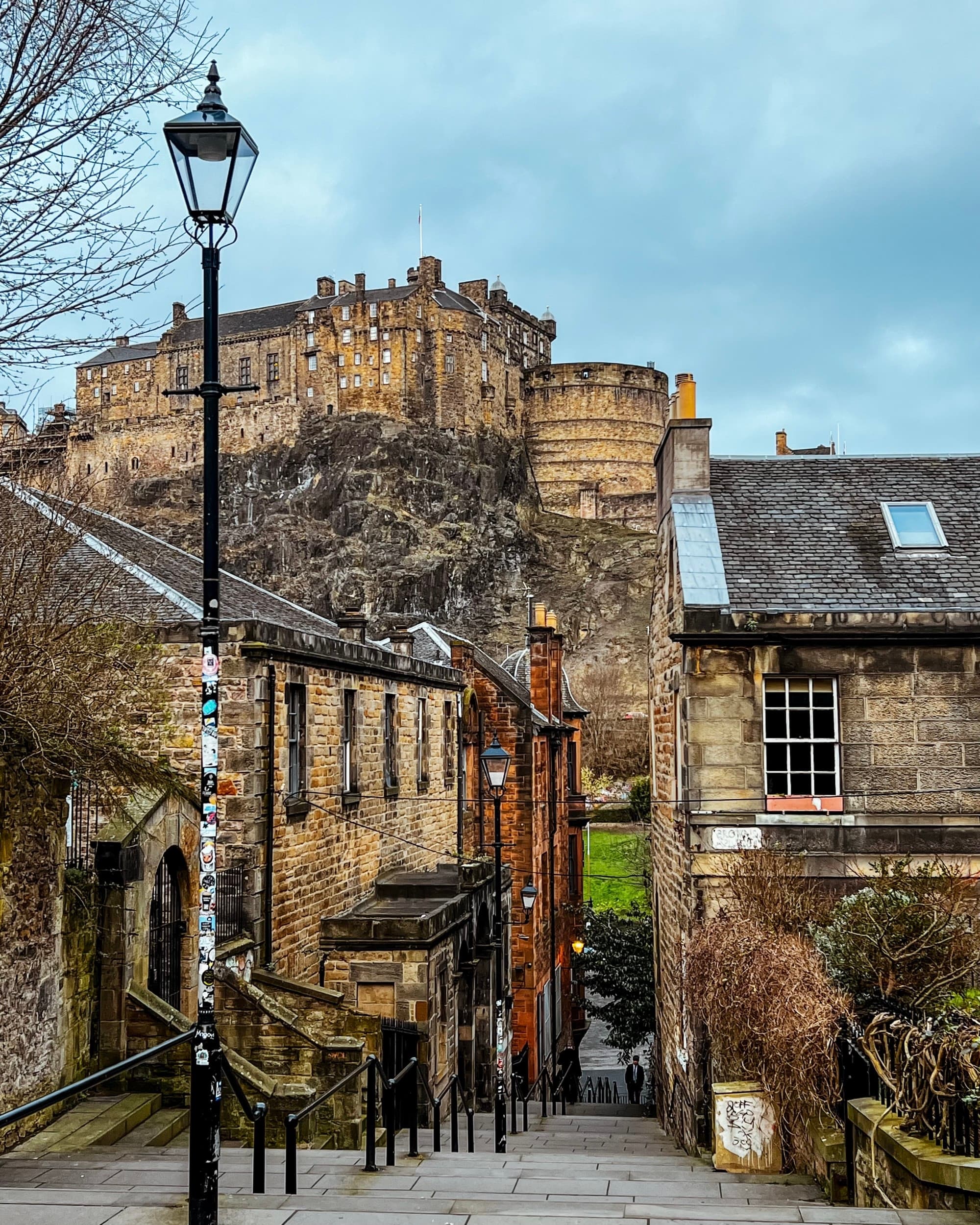 Historic stone buildings line a a quiet corner of Edinburgh under a cloudy sky.