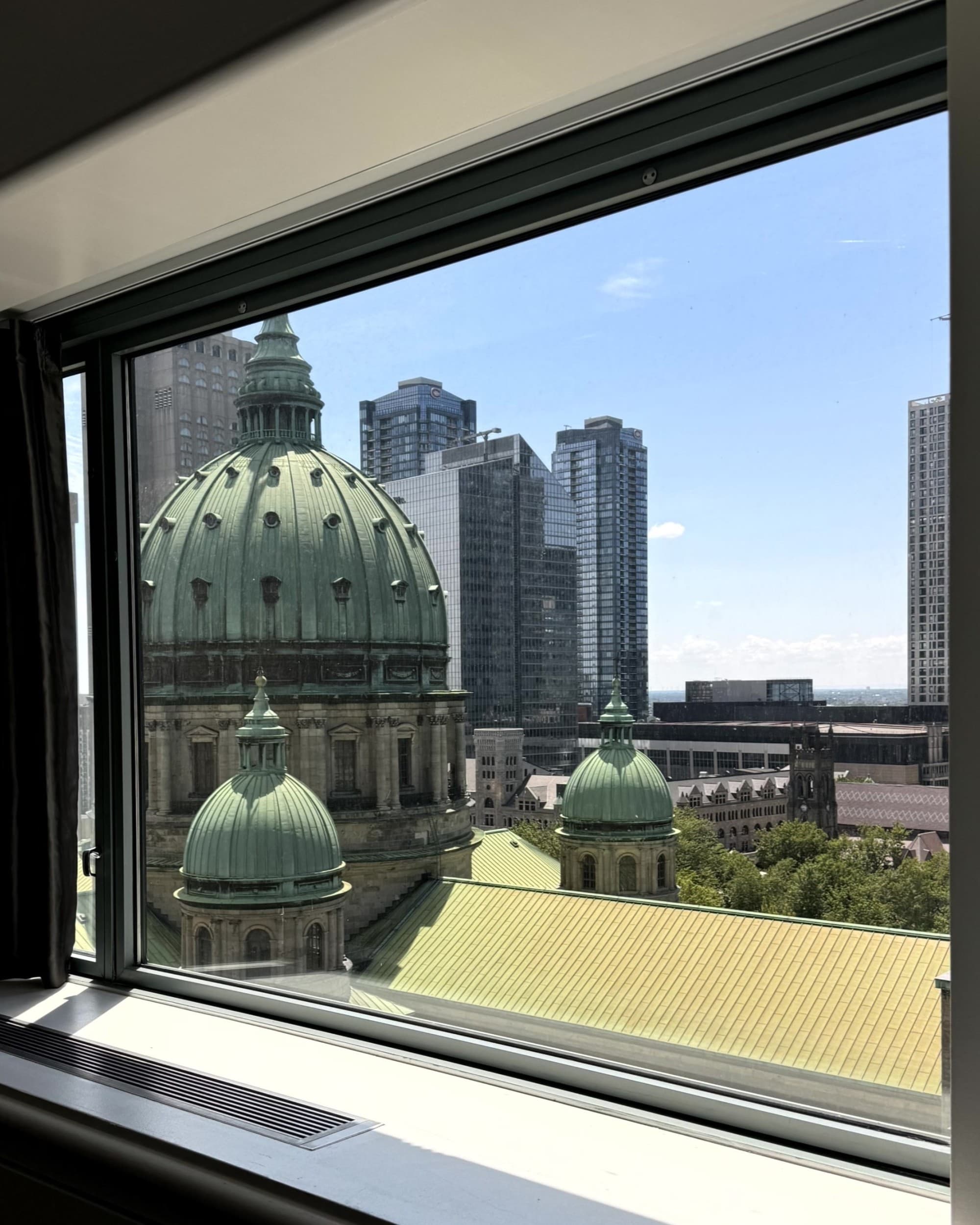 View from window of the city and skyscrapers as well as three large green domes during the day.