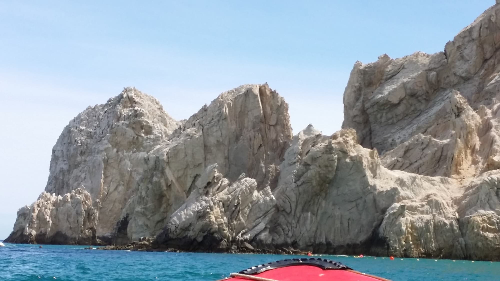 Rocks rising out of the water surrounded by lapping waves on a clear day.