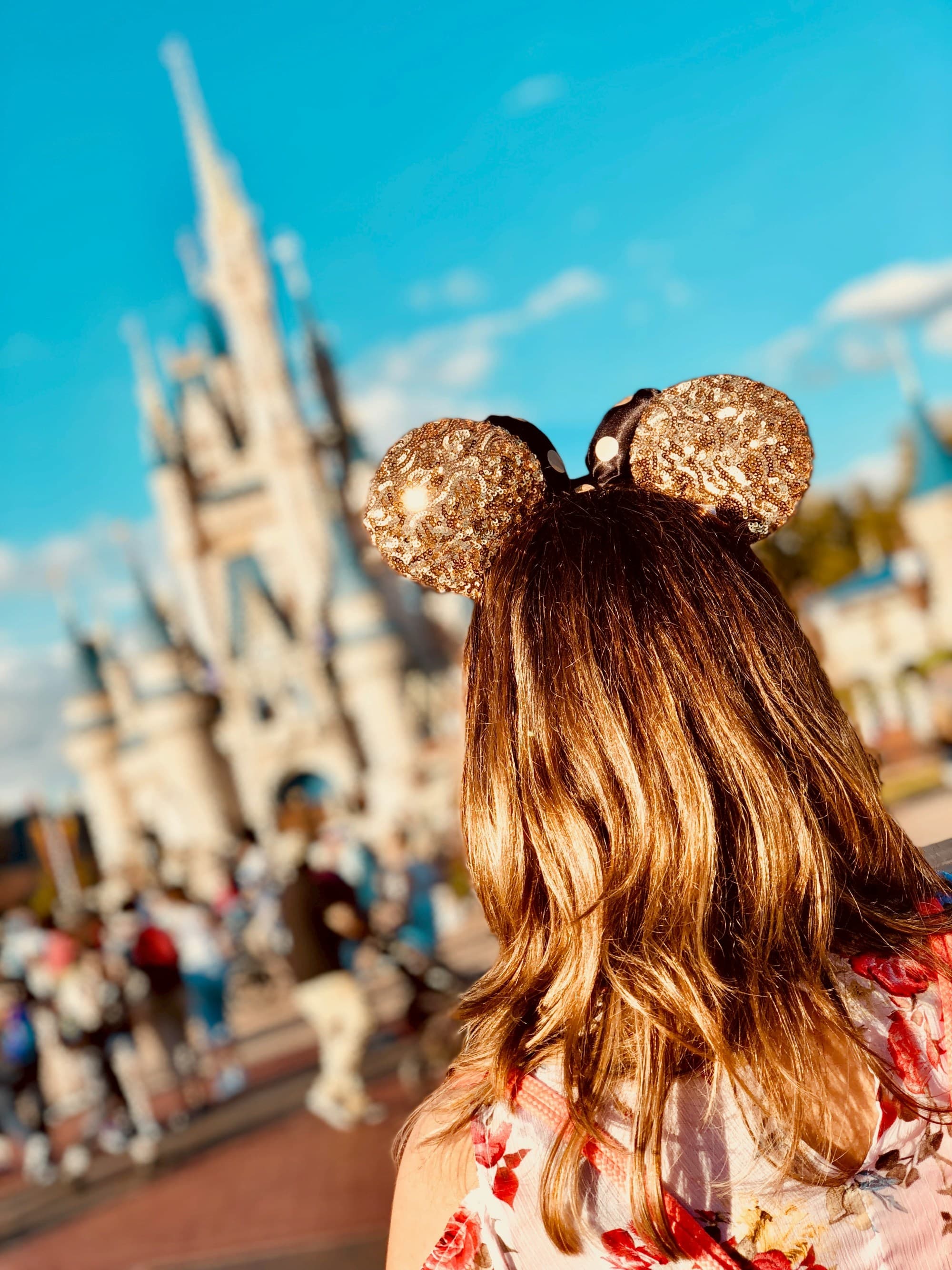 A woman wearing golden Mickey Ears at Disneyland with the castle blurred out in the background.