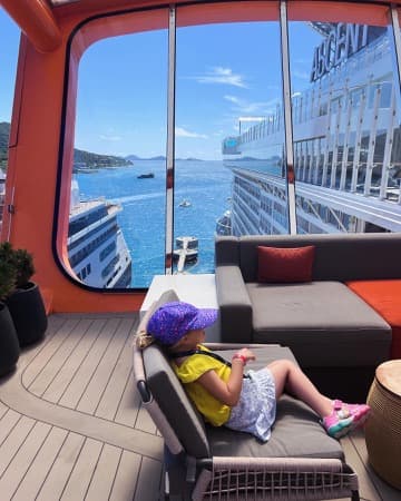 Nicole's daughter sitting on a couch on the ship with a window overlooking the ocean.