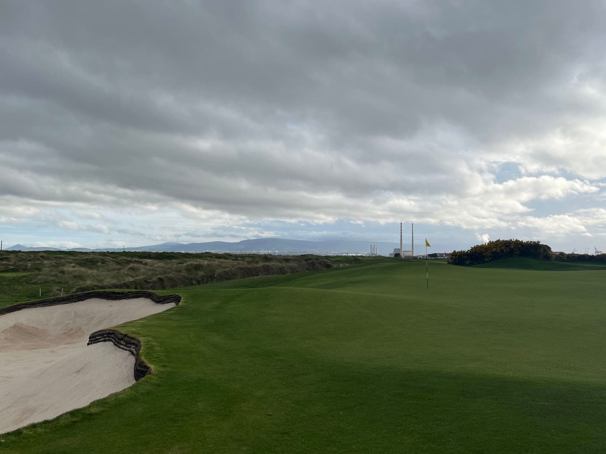 A green golf course and sand pit of a golf course on a cloudy day.