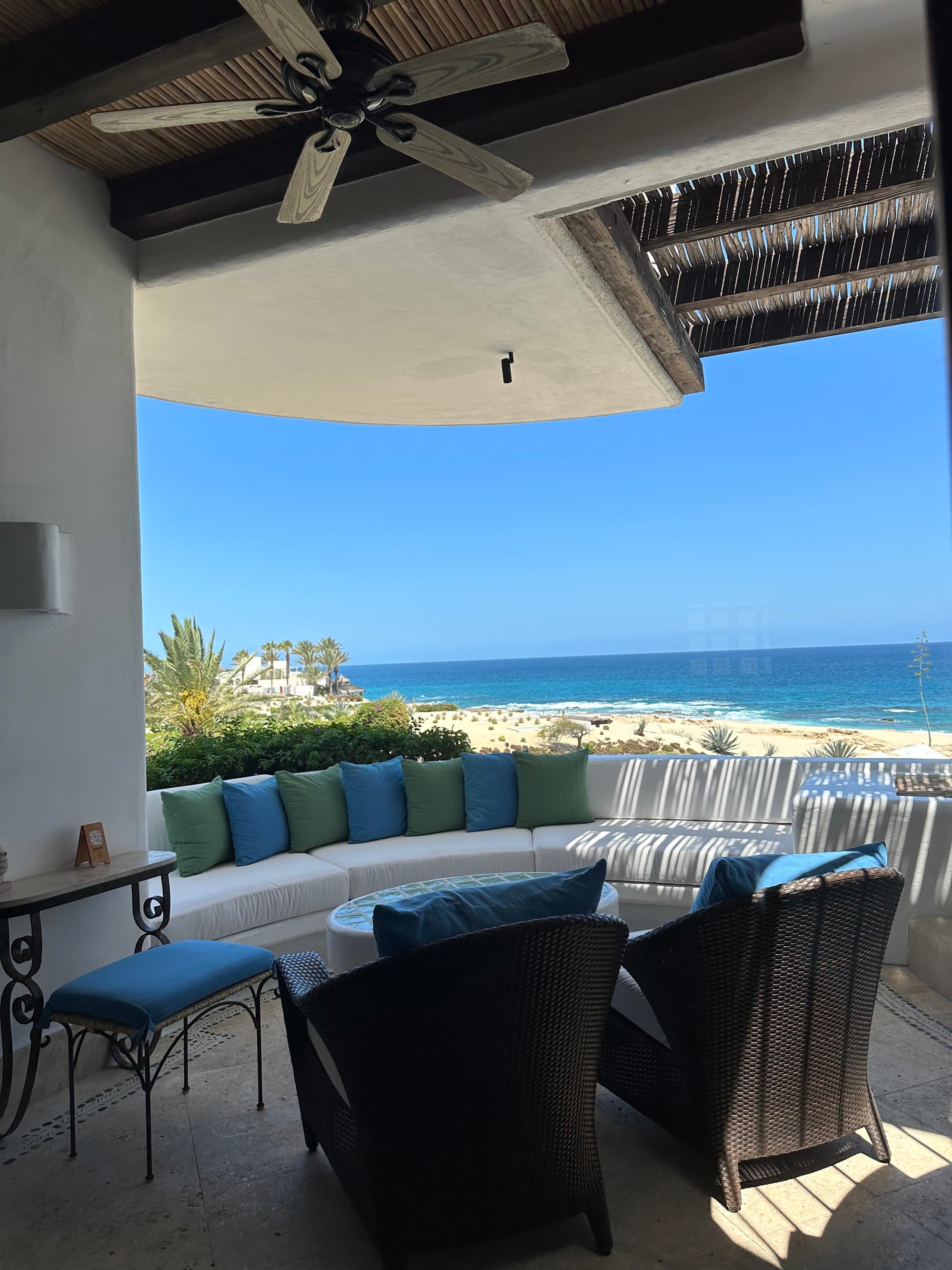 A cozy seating area of the hotel room's balcony with a view of the beach on a sunny day.