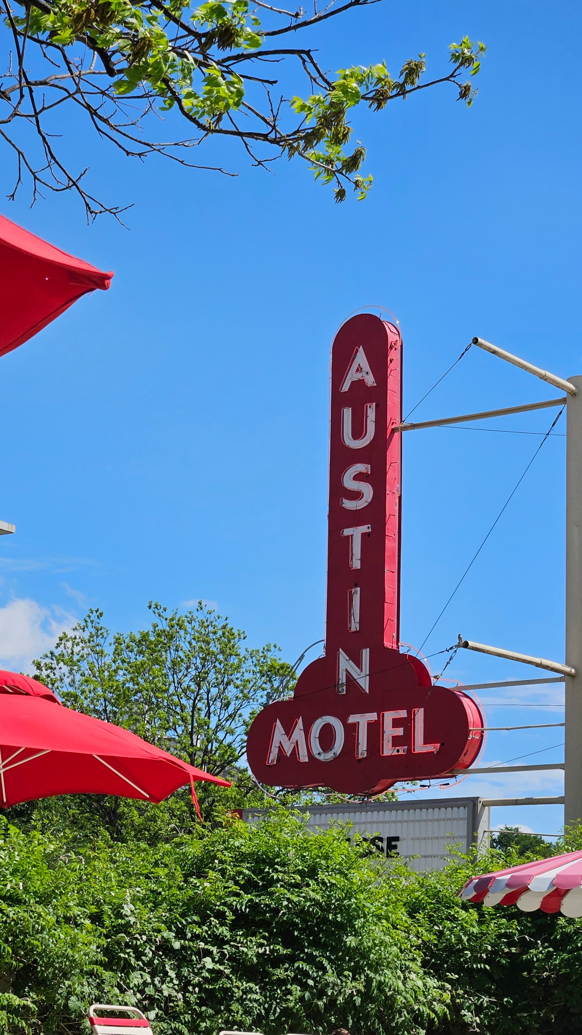 The Austin Motel exterior sign, a red sign near green trees and red umbrellas - Nicole Diez