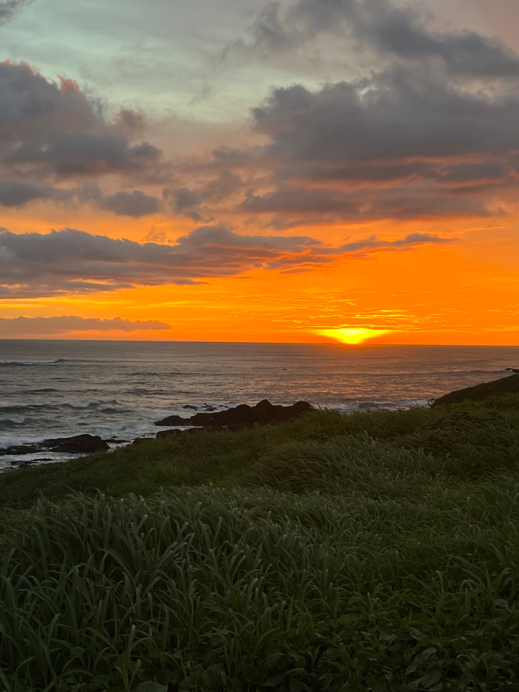 A blood-orange sunset over the sea and grassy land.