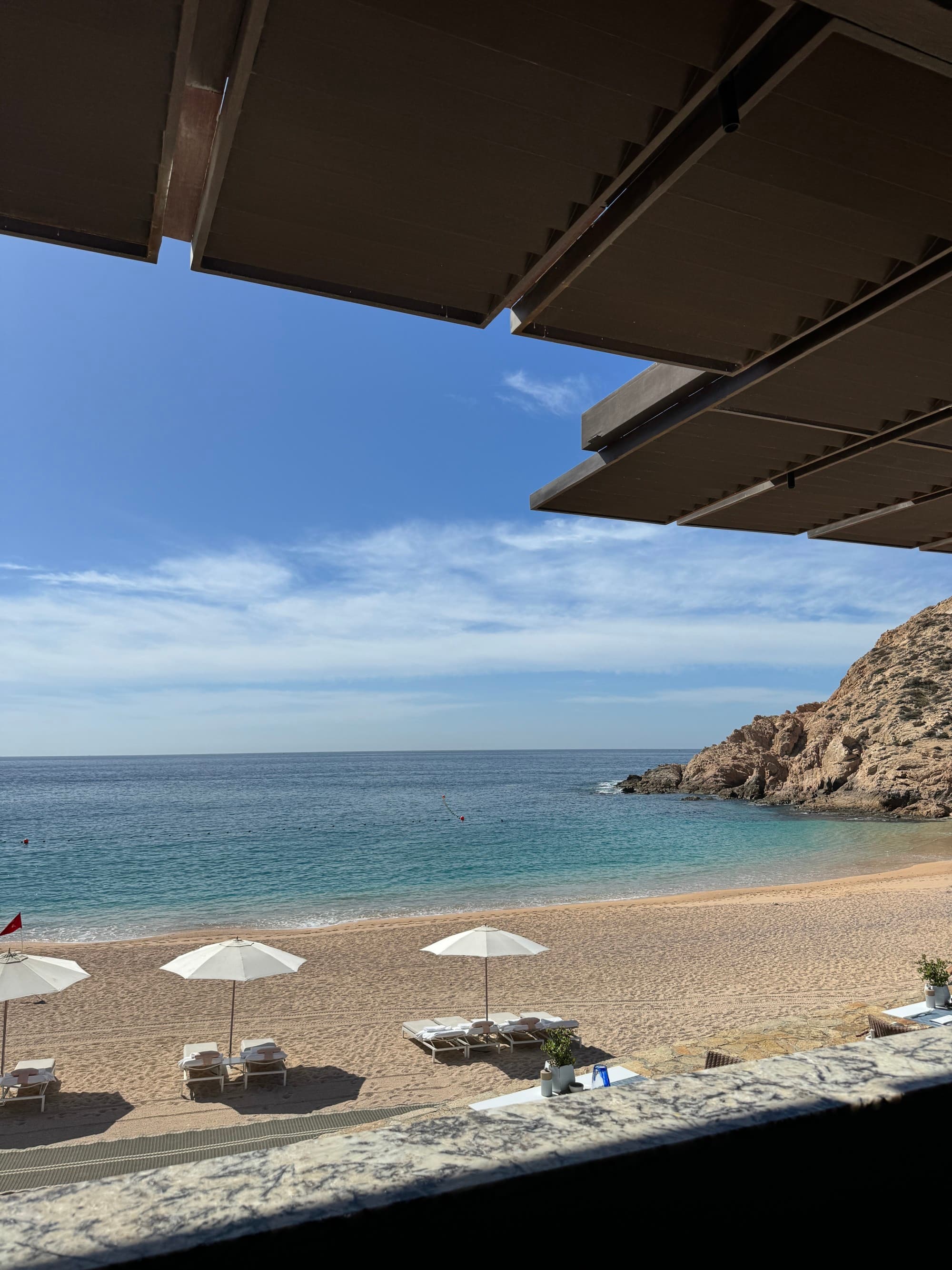 A view of a small beach with a few chairs and umbrellas, and a rocky coast on the side on a sunny day.