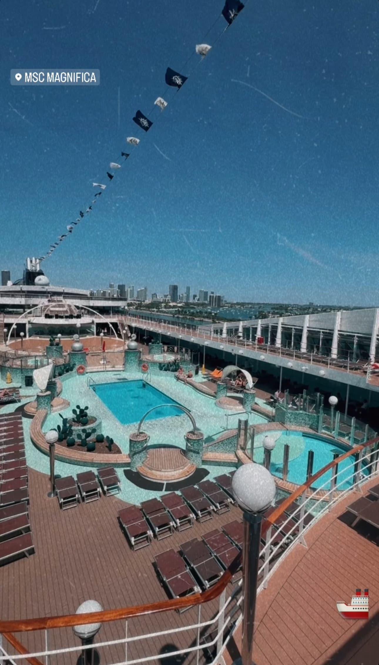 An aerial shot of a cruise ship's outdoor pool area with two pools, lounge chairs and shaded areas.