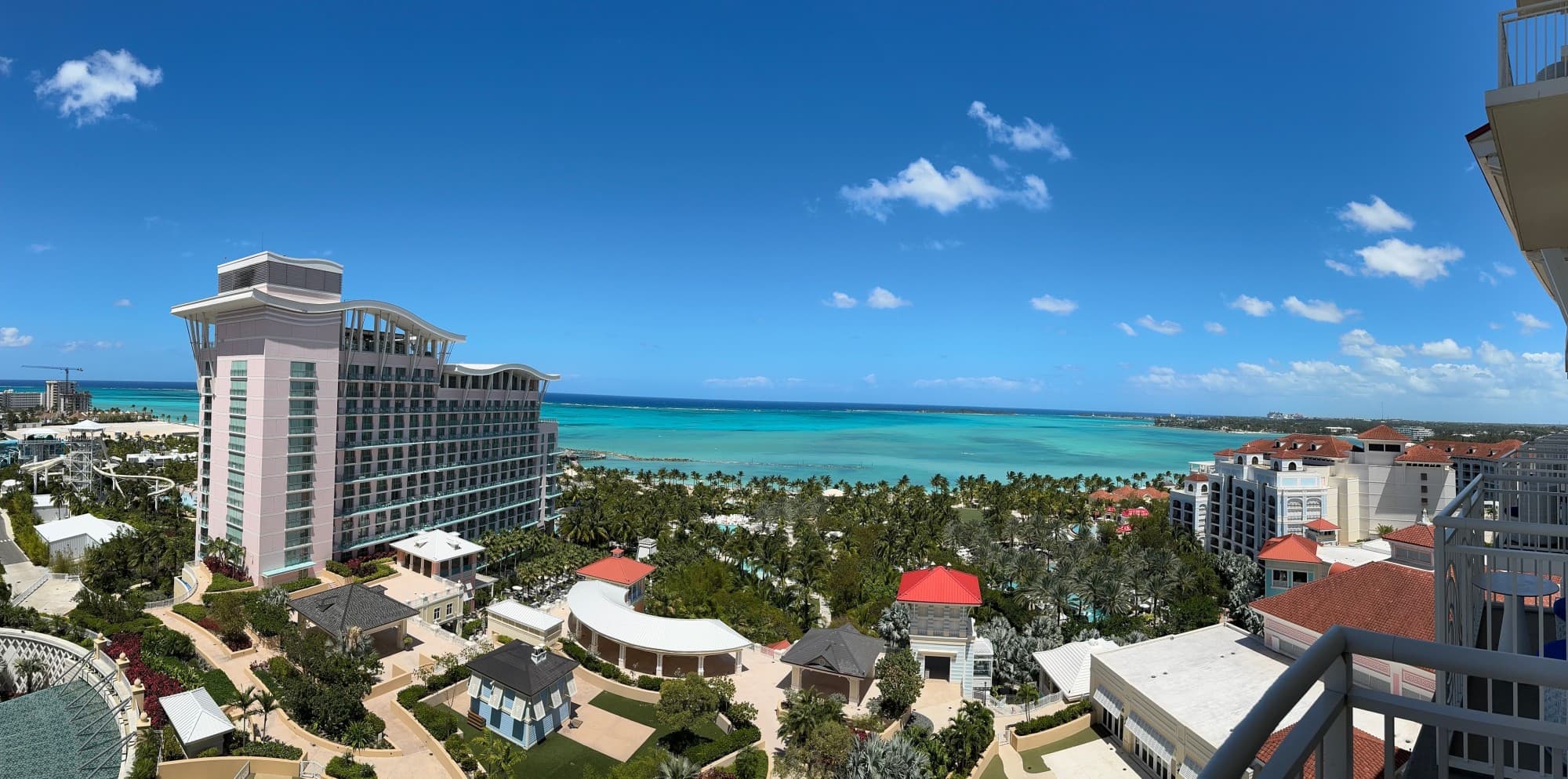 This image depicts a panoramic view of a coastal city scape with trees, buildings and light blue water in the distance.