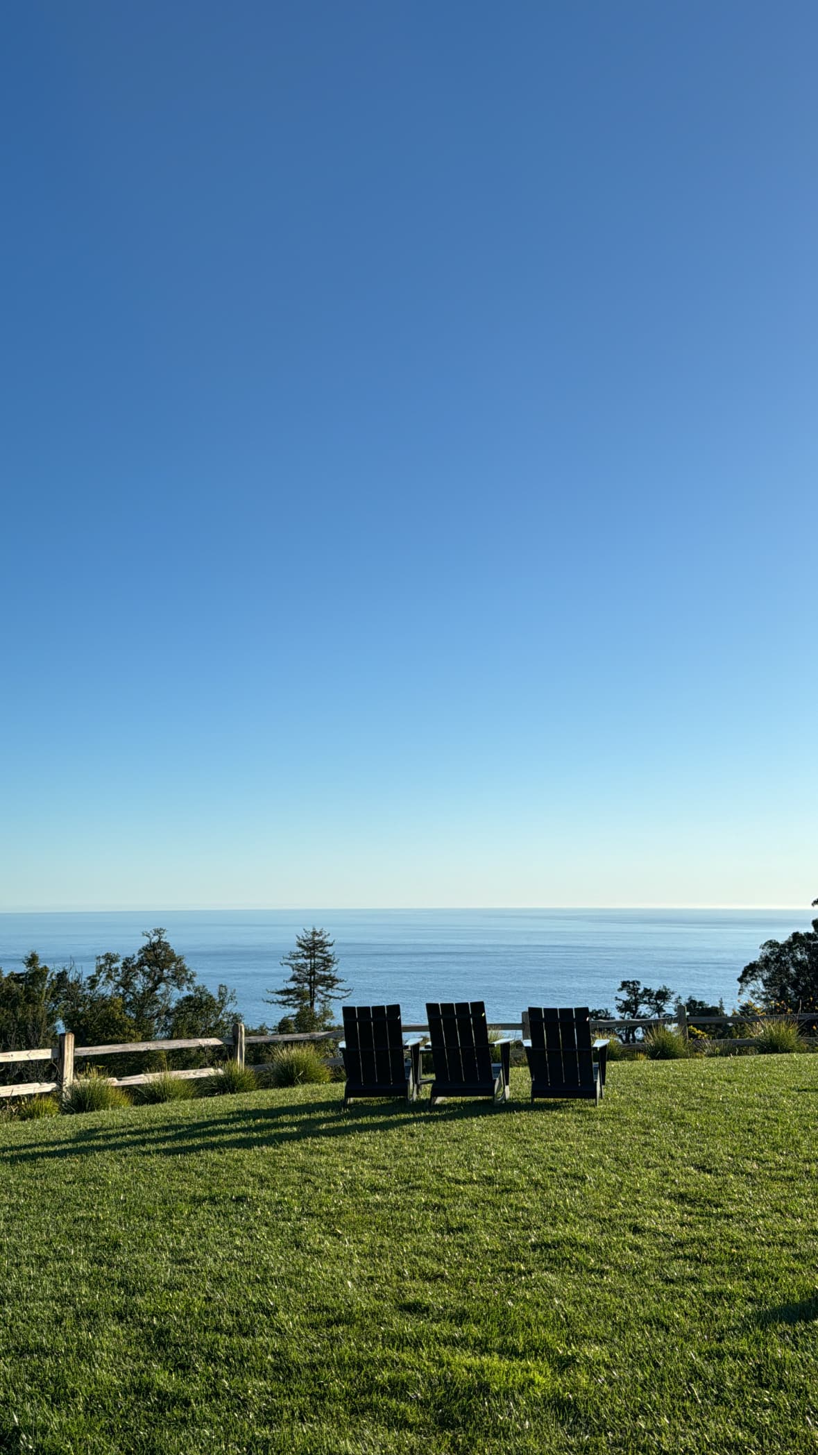 A view of three chairs on a grassy lawn with a view of the blue sea.