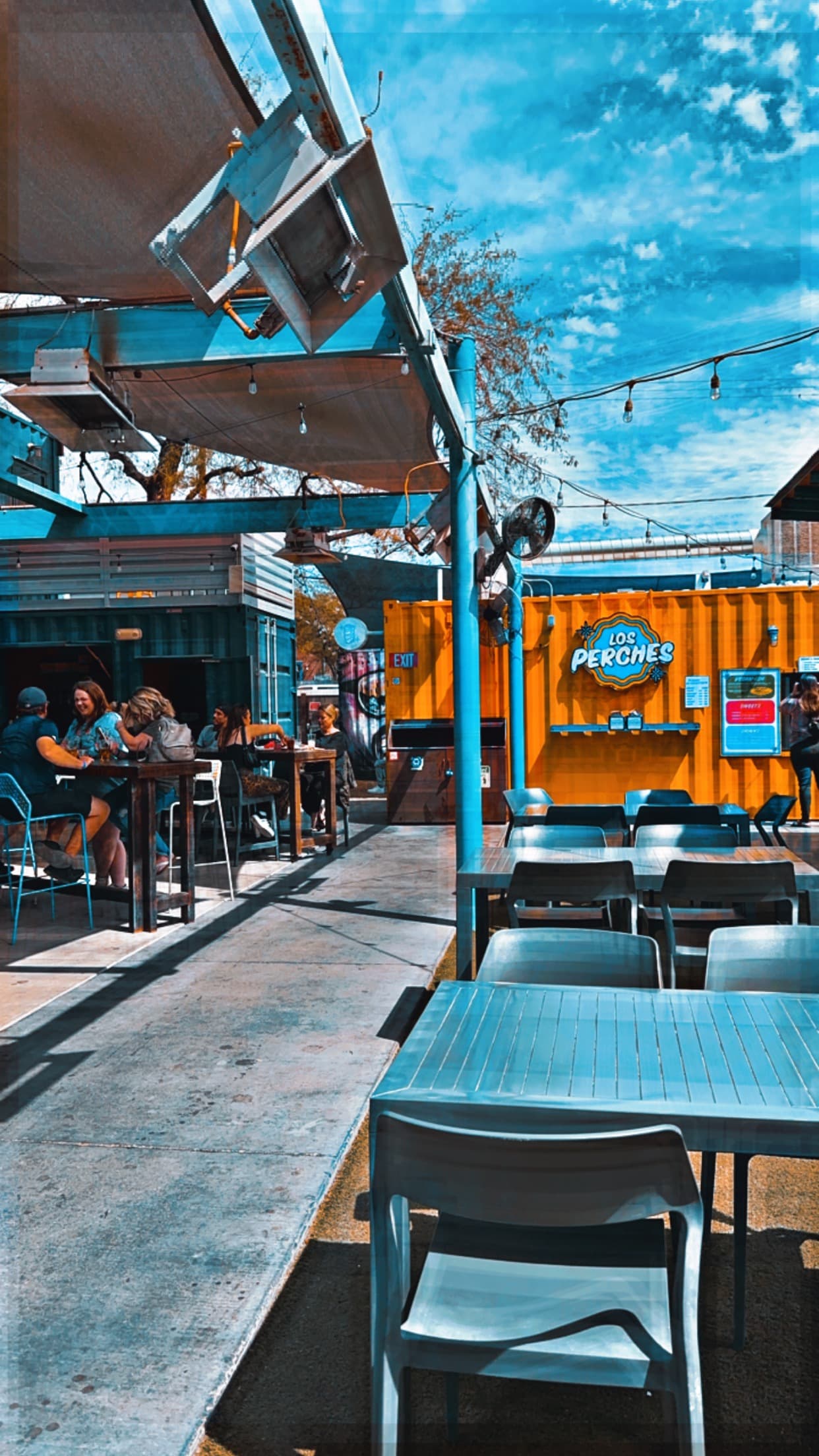 An outdoor patio with tables, chairs, string lights and a sign in the background.