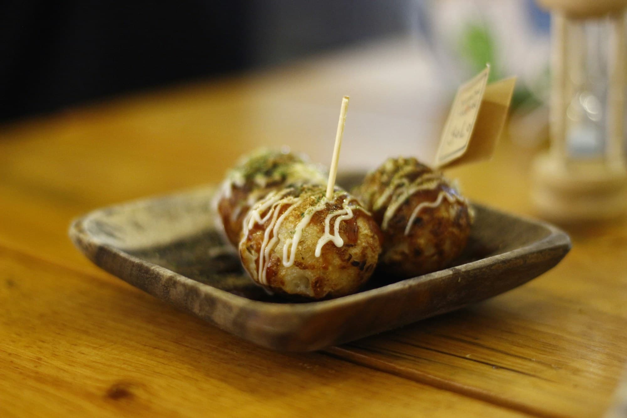 A wooden table with a plate of a savory balls of batter filled with diced octopus, a typical Osaka street food.