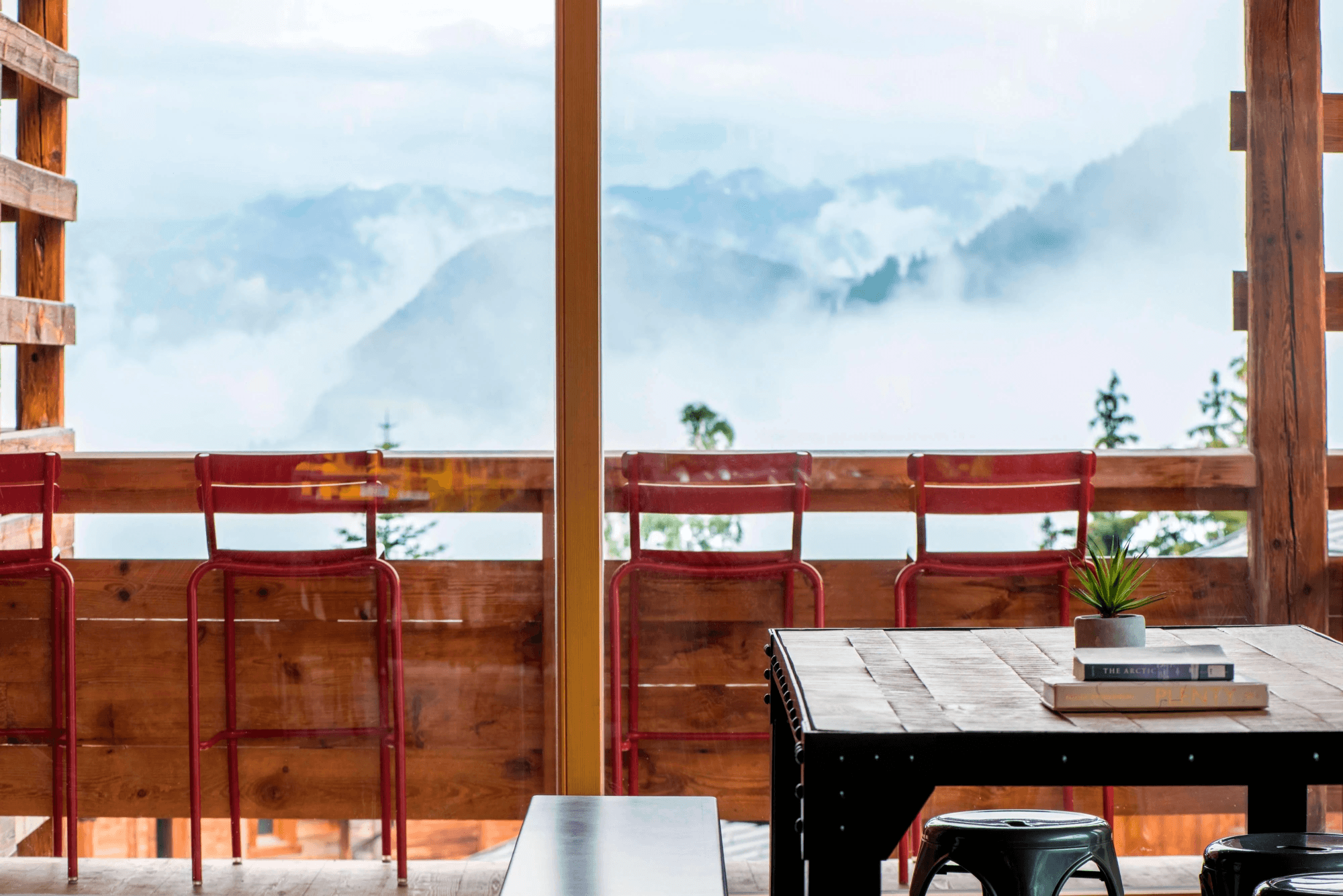 A black table and red stools against a wooden ledge with mountains and clouds in the background.