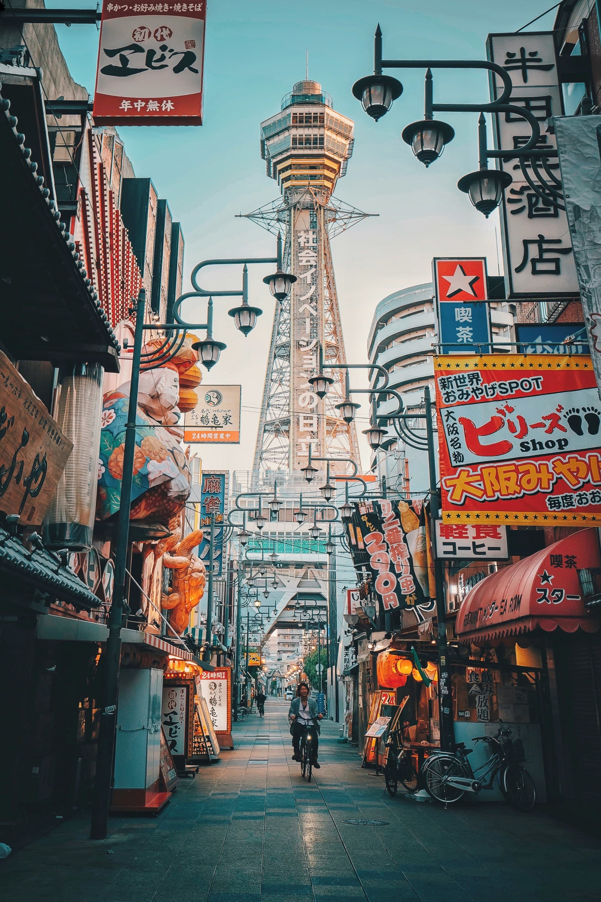 A low-angled view of a city street with colorful billboards and a tower in the distance