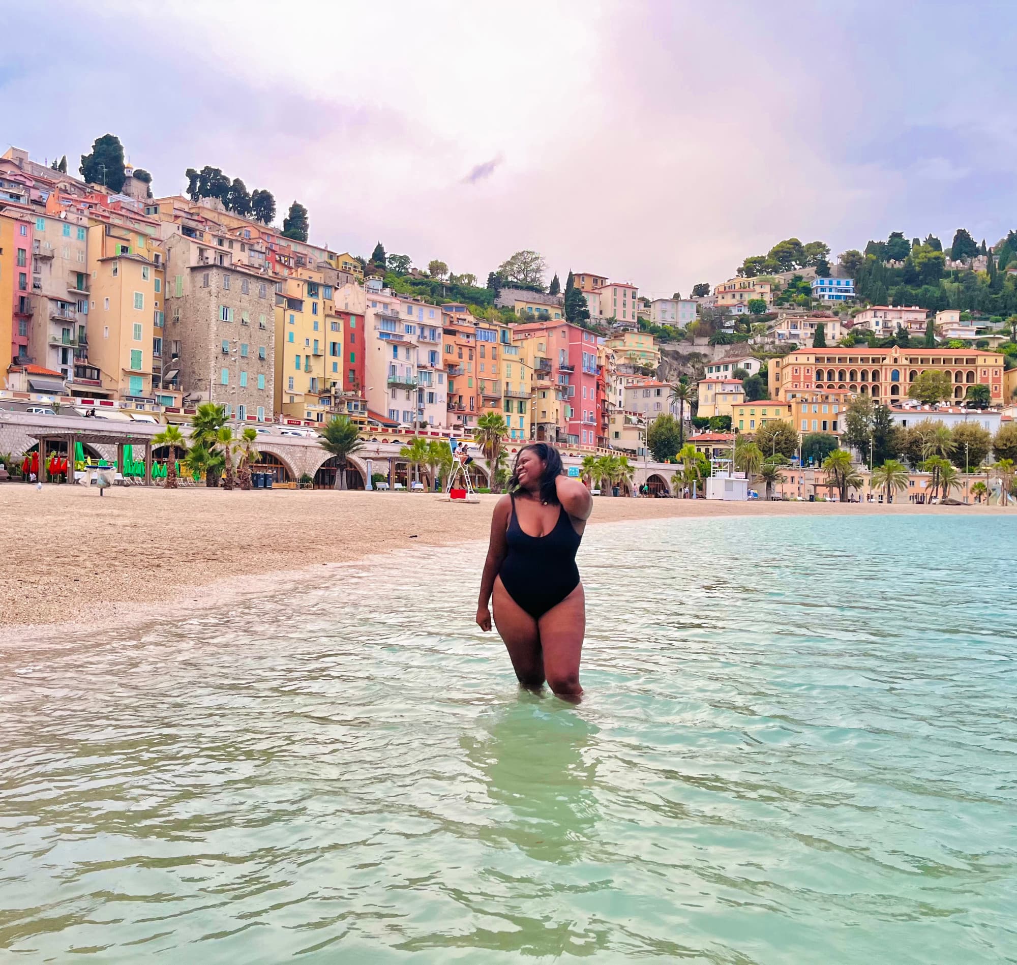 Travel advisor posing in the ocean with a lovely colorful beach town in the distance