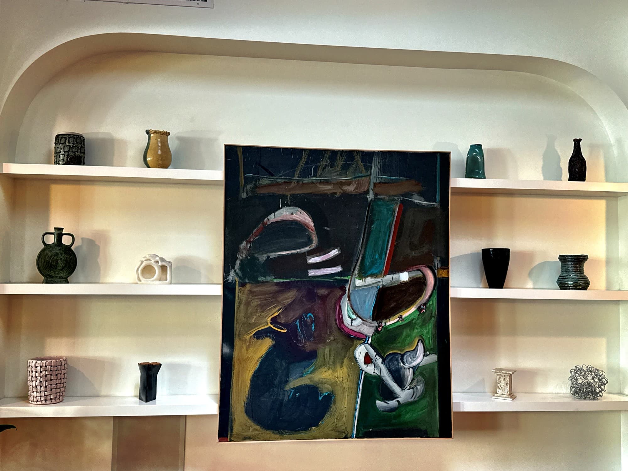 A beautiful hotel lobby with abstract artwork hanging in the middle of shelving units showcasing various ceramics.
