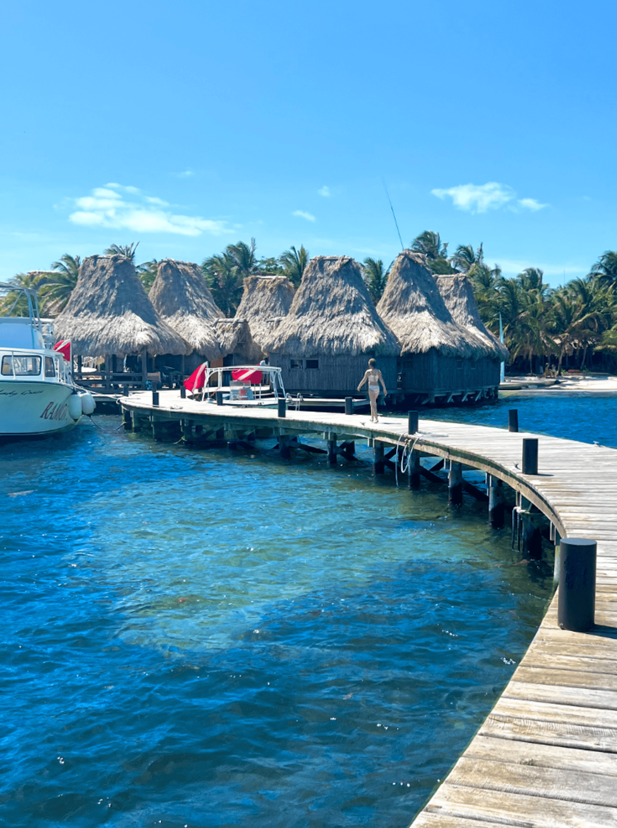 A dock in the ocean leading to suites on the water with a boat in the distance.