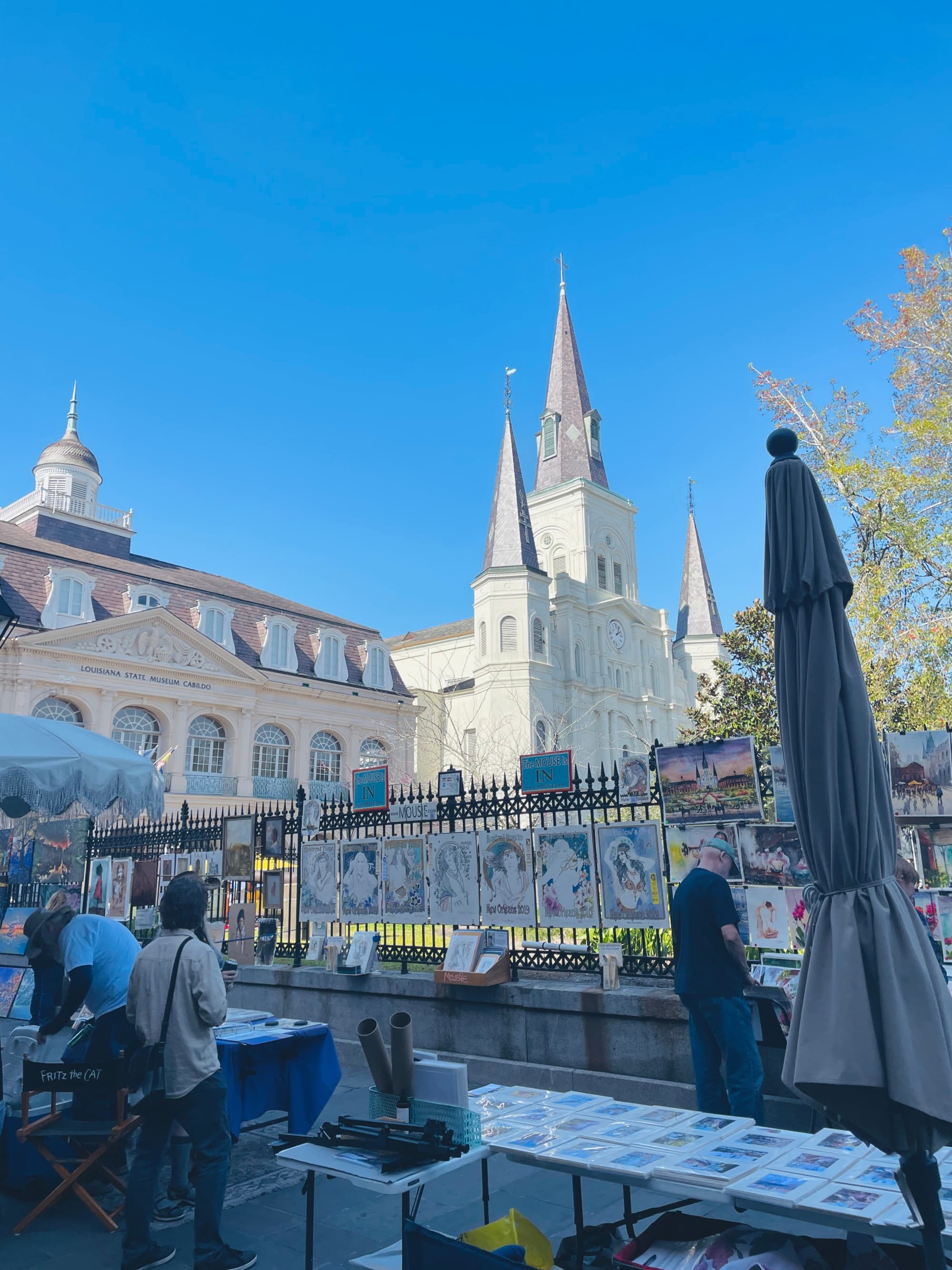 A bottom up view of old architecture, complete with pointed towers and a metal fence. There are also people and umbrellas in the forefront.