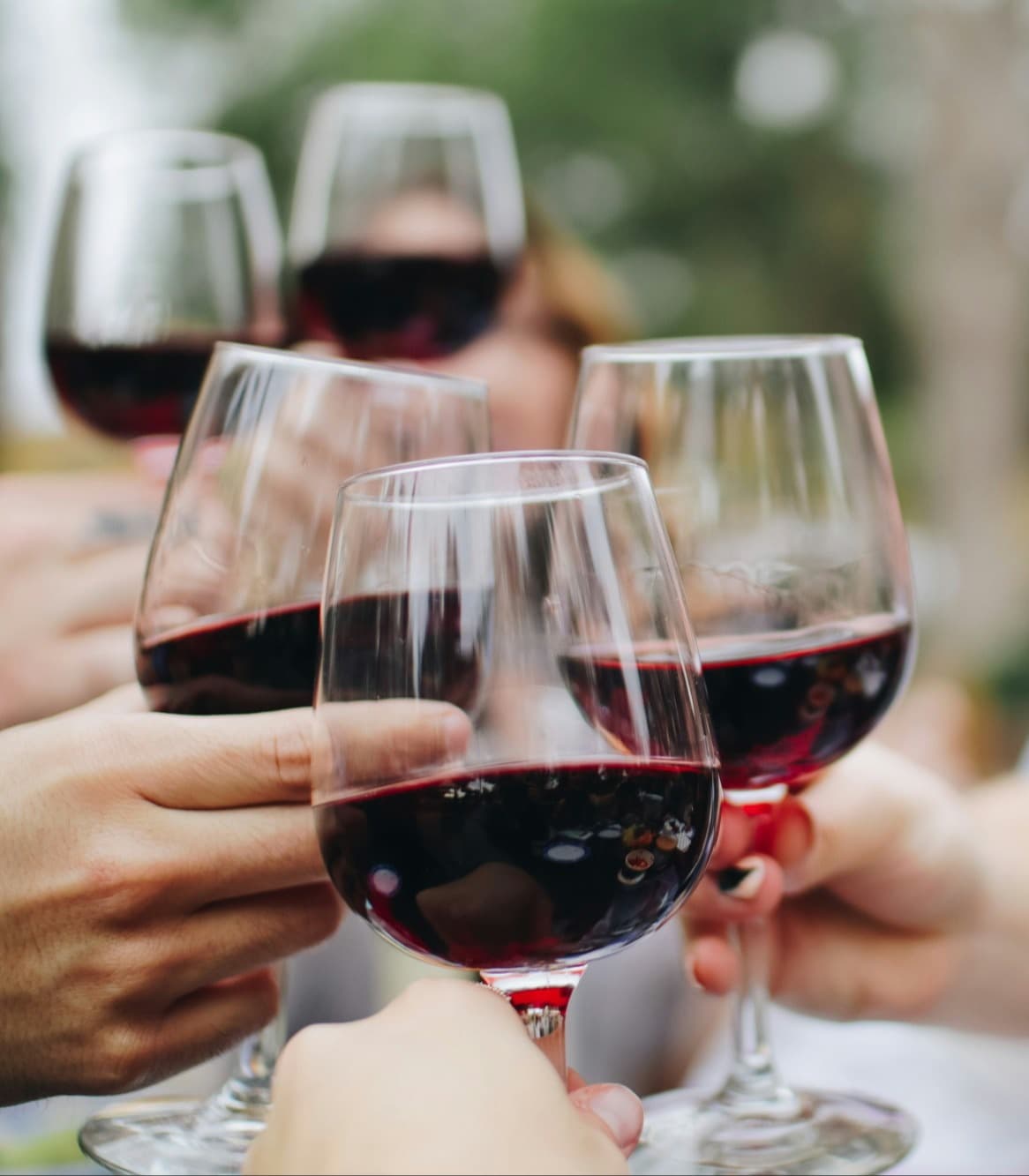 A group of people holding red-filled wine glasses together to cheers one-another.