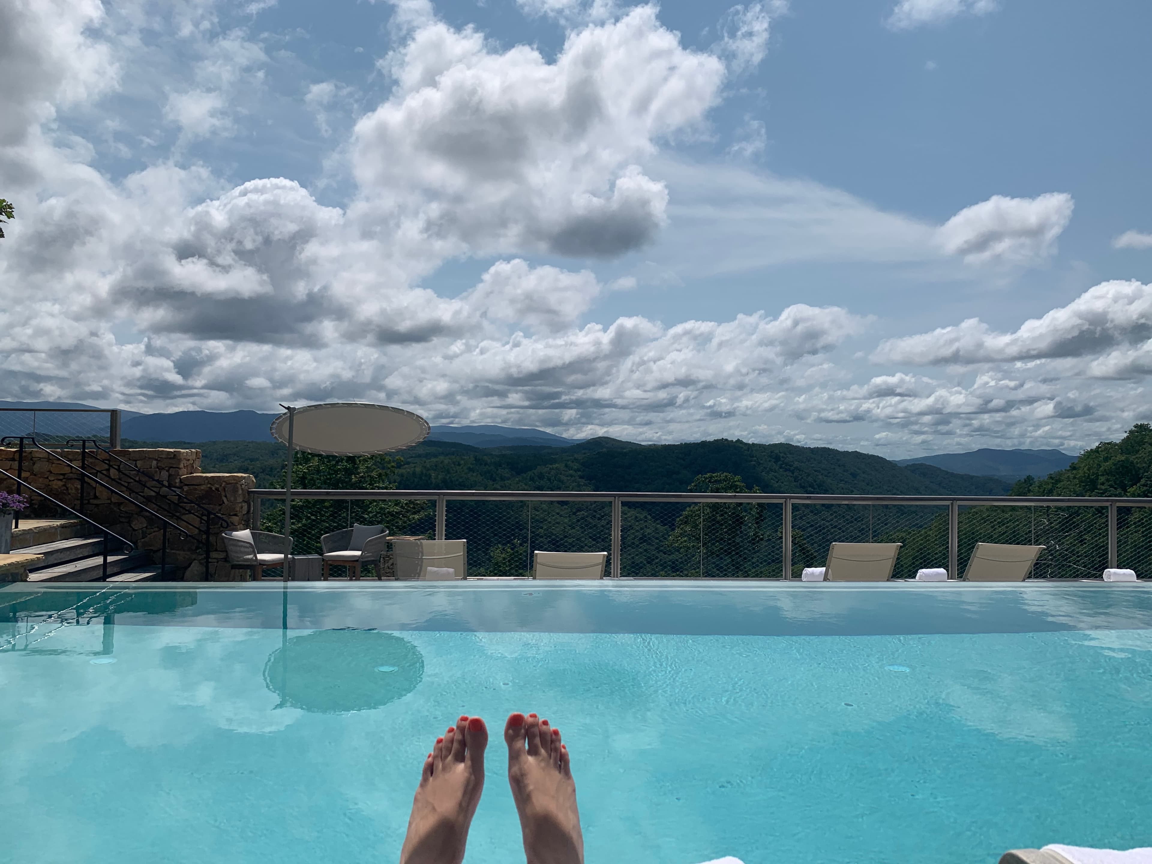 feet in front of a blue pool overlooking a lush, green valley