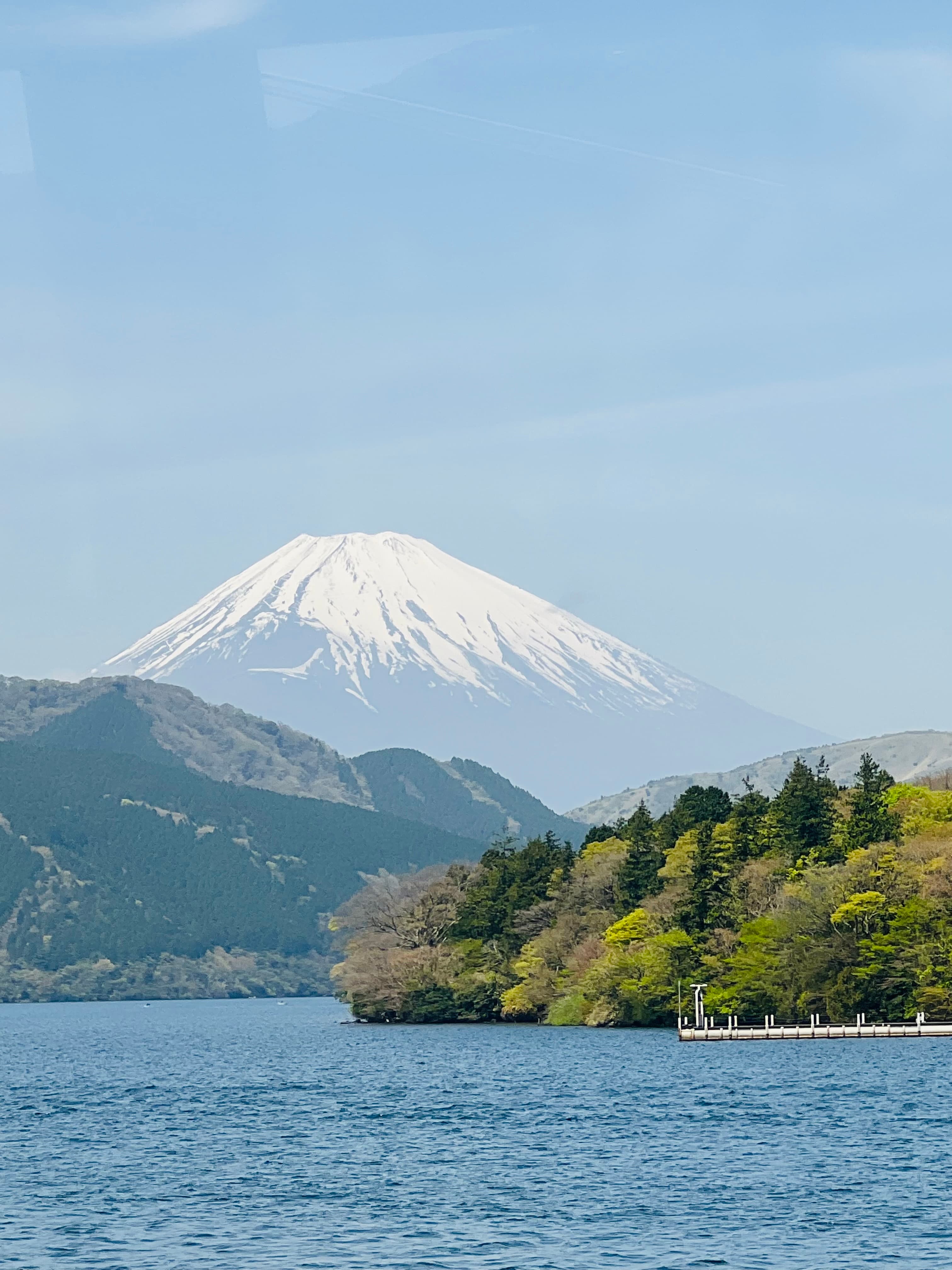 a blue lake and green tree covered coast line in front of a snow-capped mountain