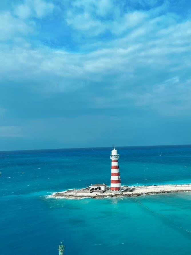 An image of a light house on a sandy jetty with a clear blue ocean on a sunny day