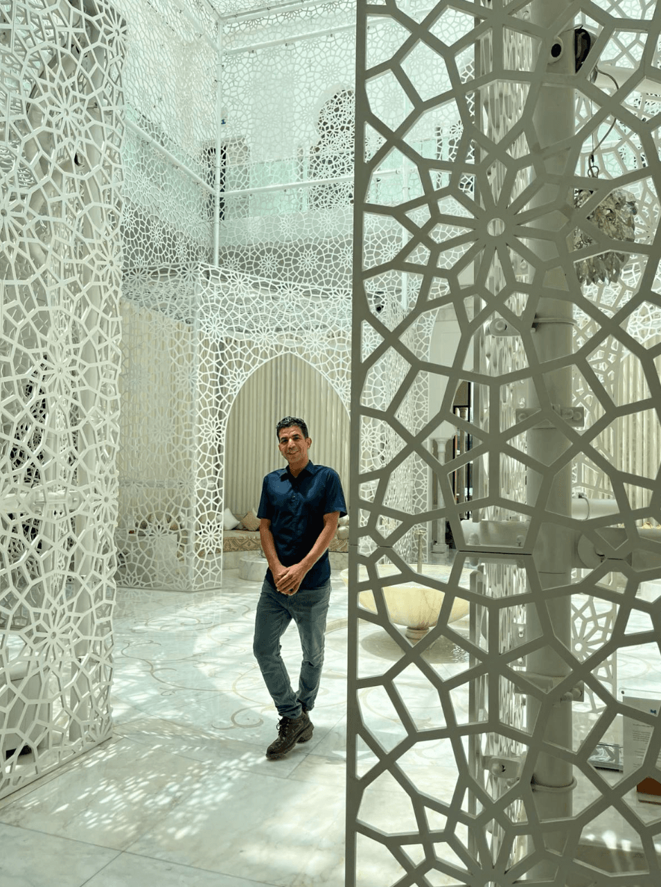 A man standing in a beautiful room with white detailing and intricate patterns along the walls and floor.