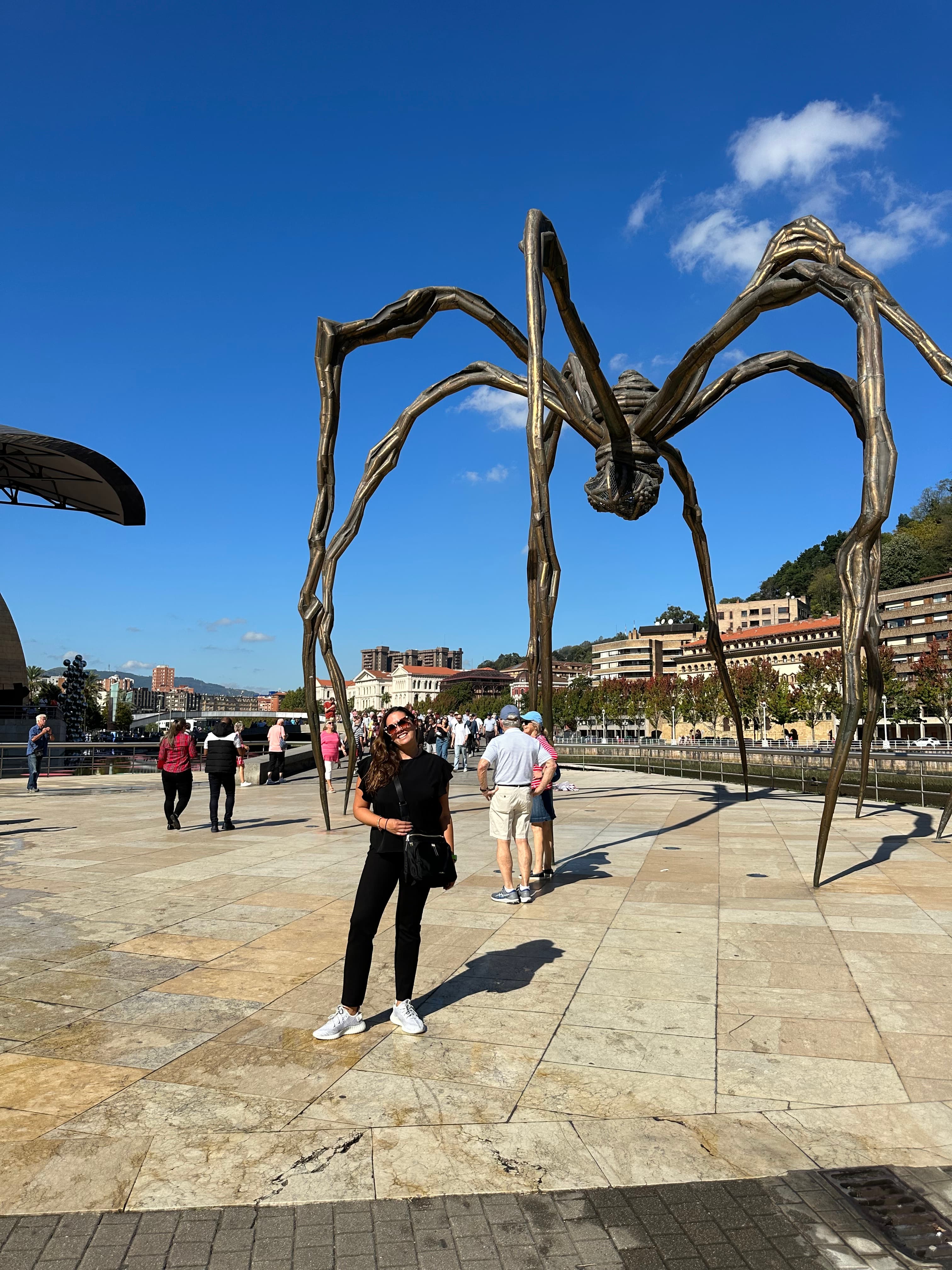 Travel advisor Andrea posing in front of Maman spider-shaped sculpture with other people in view on a sunny day