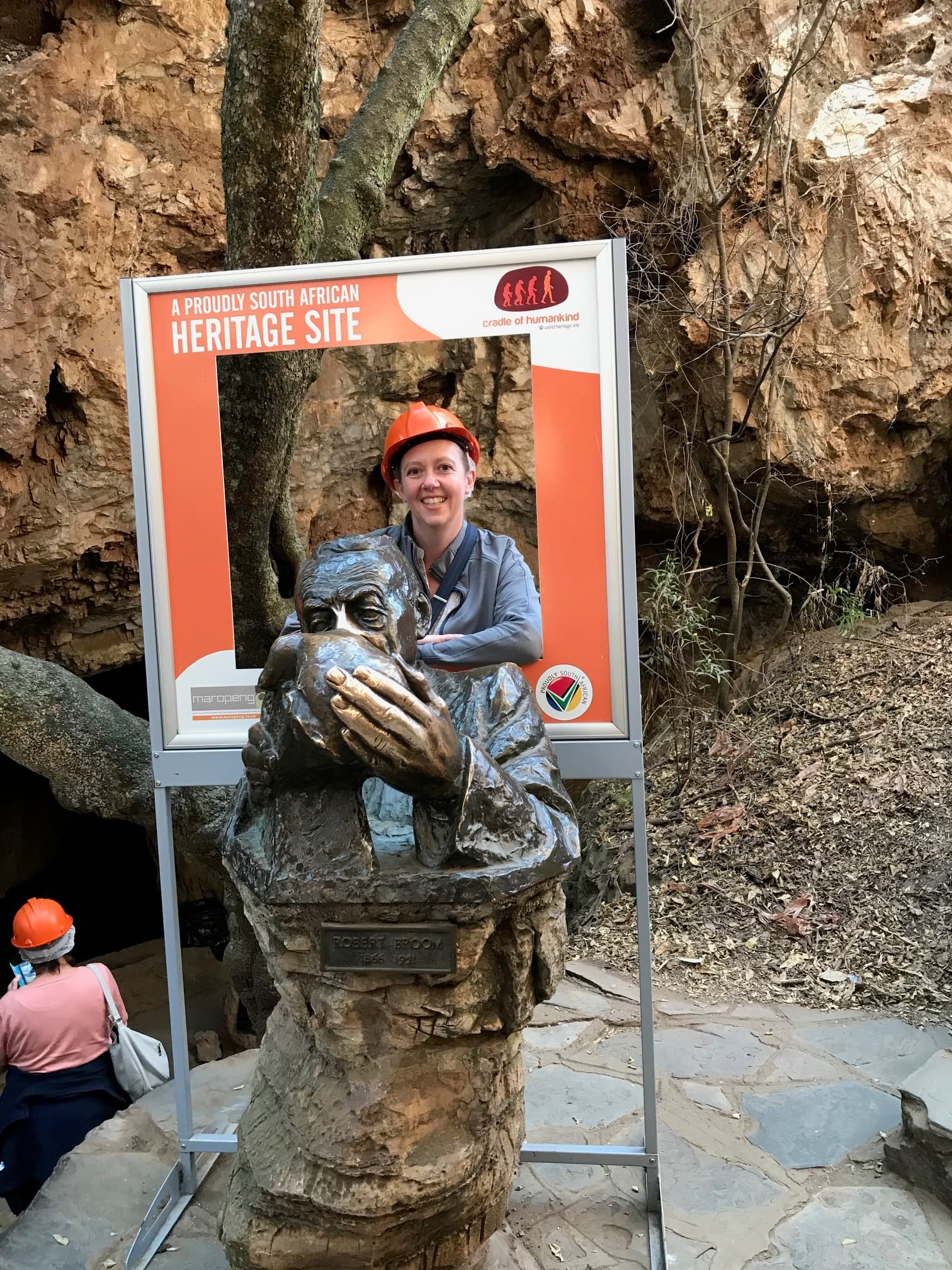 Travel advisor Tammy in an orange helmet posing with photo props and a statue outside with rocky landscape in view
