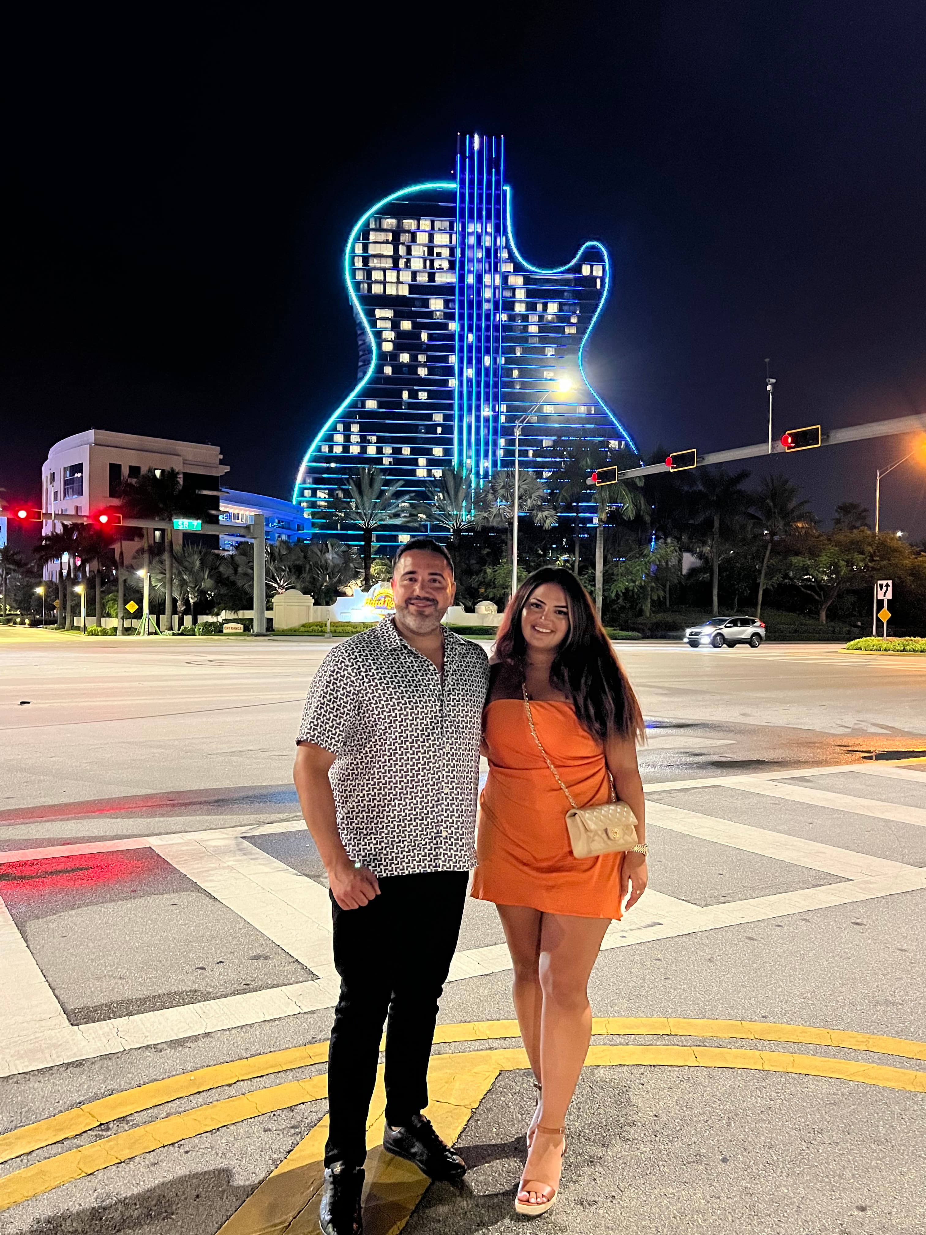 Travel advisor Riva Hannah posing for a picture on the street at night in front of a building that is lit up with bright blue lights in the shape of a guitar