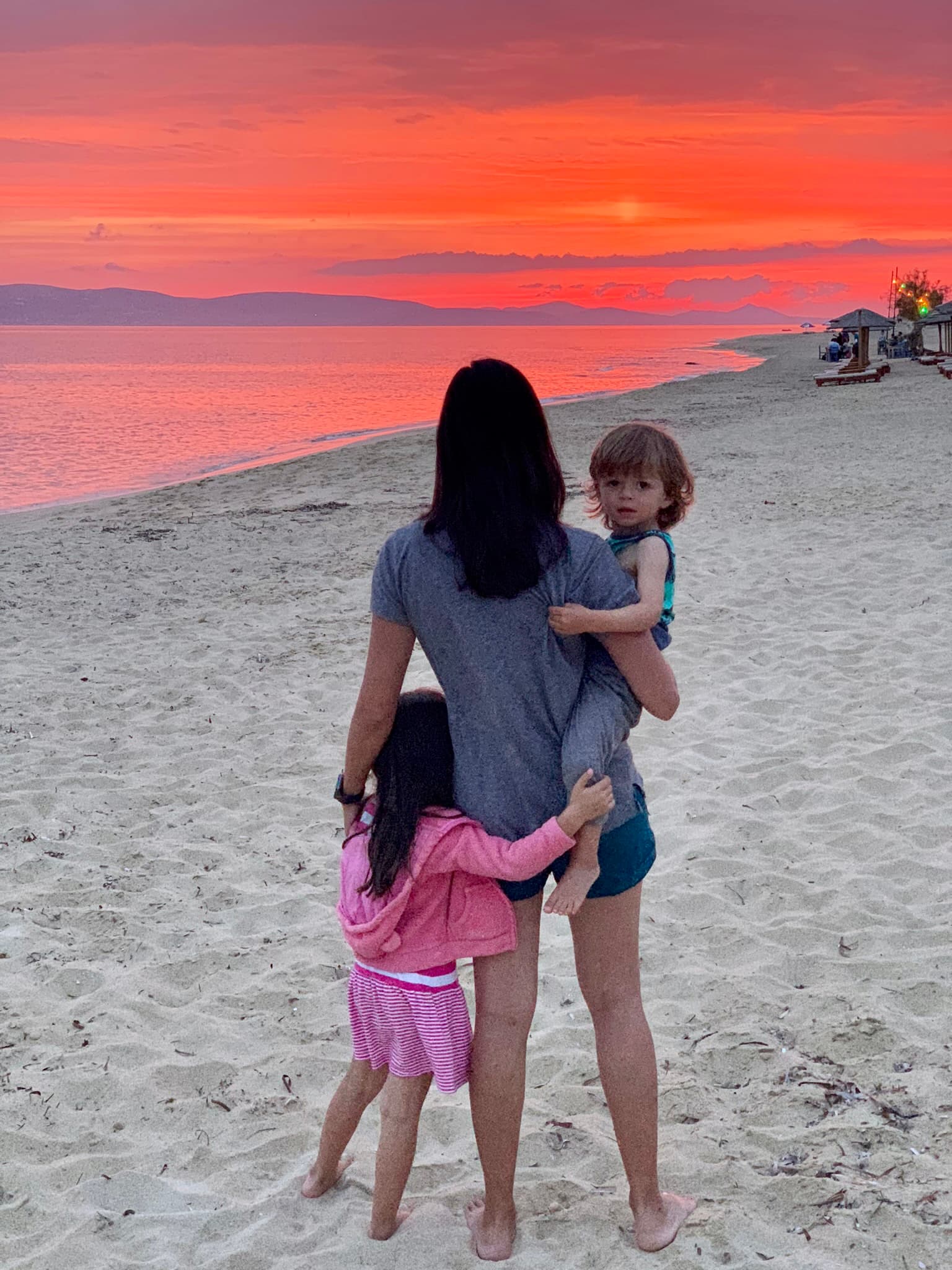 Nadiah on the beach with her children and an orange sunset in the distance.