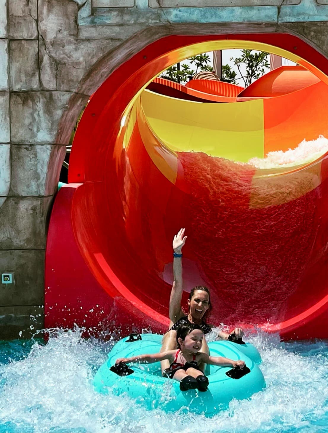 Jennifer and a child going down a red water slide.