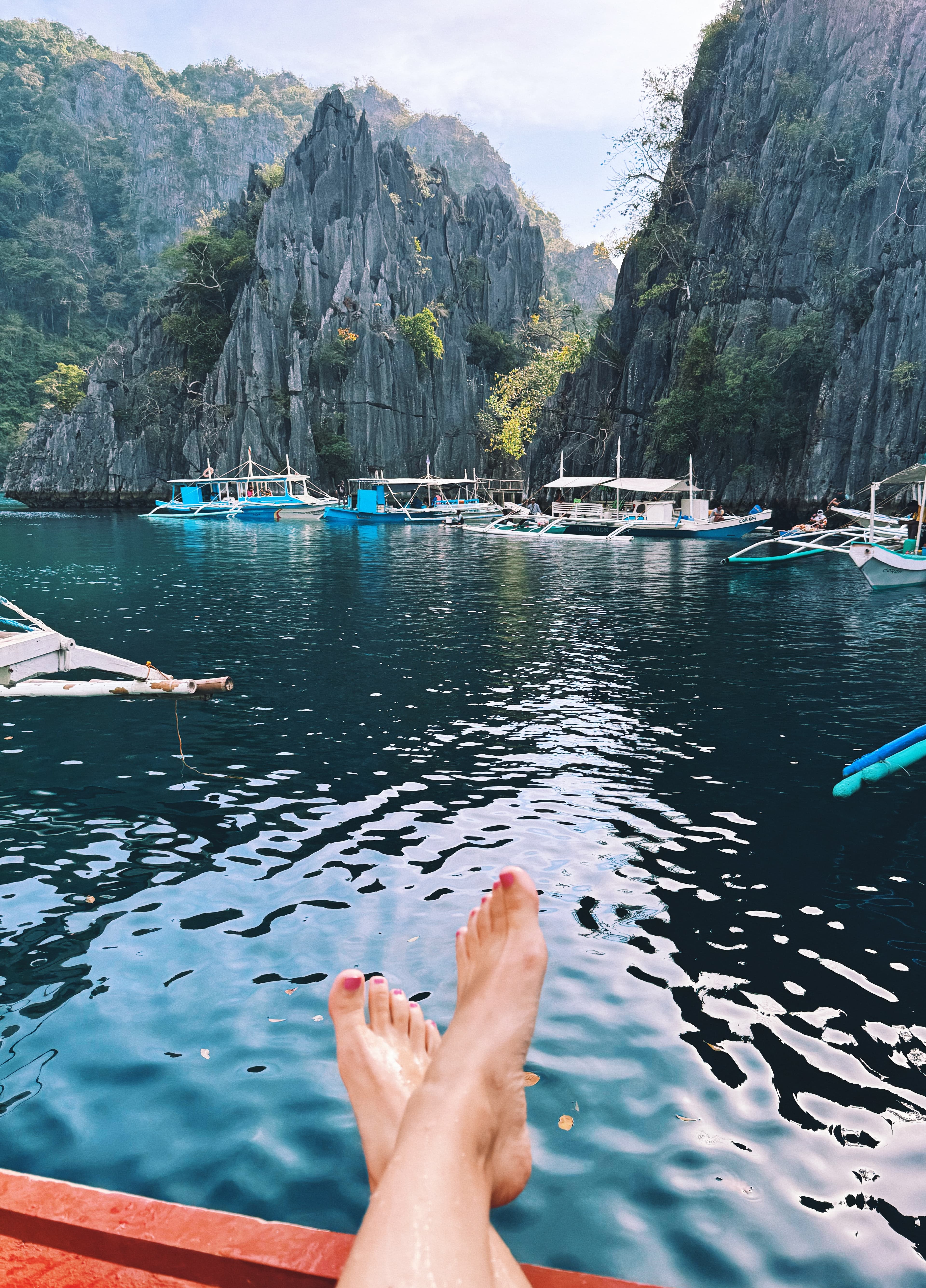 Feet outstretched in front of lake with boats and mountains in the background